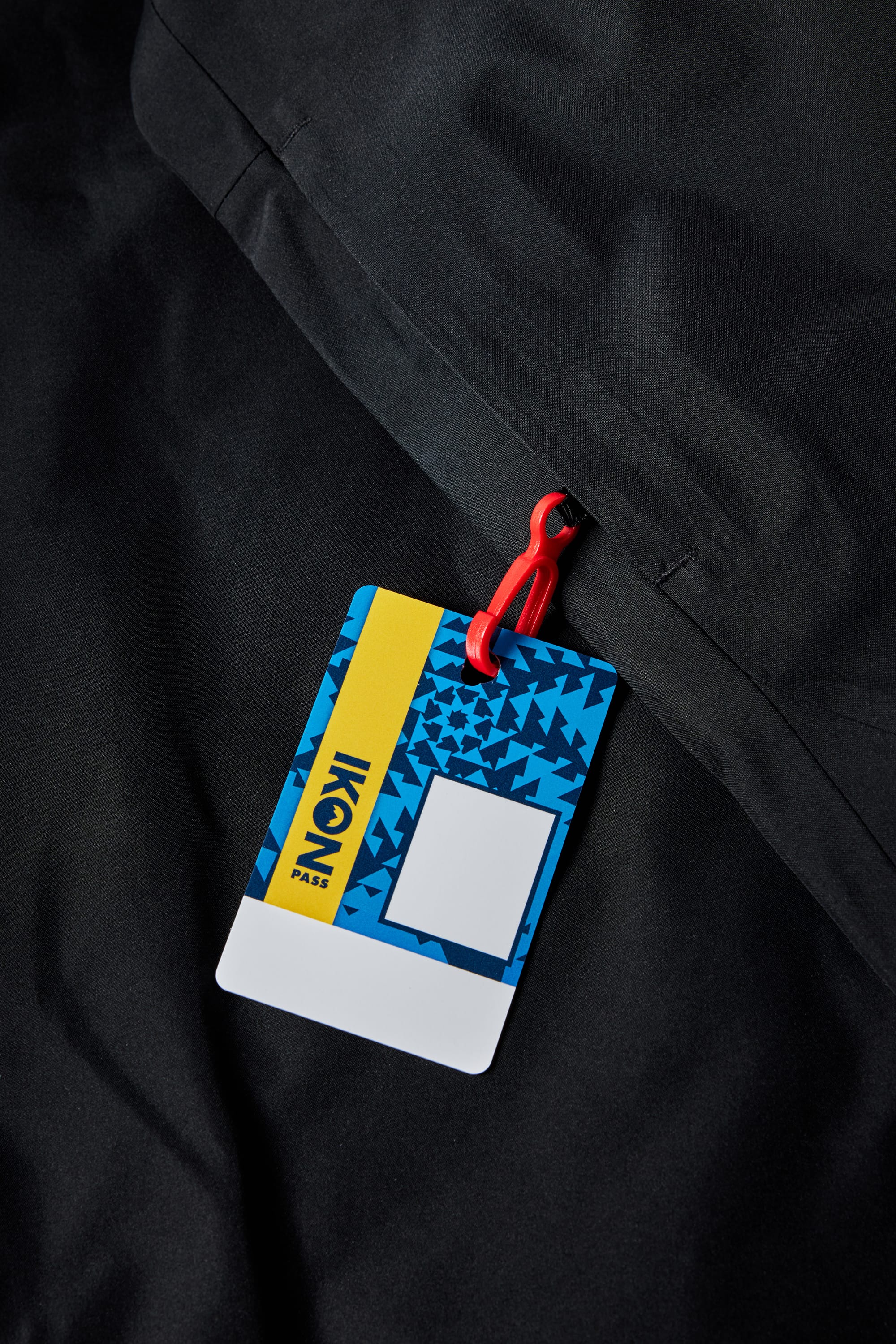 A limited edition 686 x Iron Maiden Mens Insulated Battle Jacket by 686 is shown with a blue and yellow IKON Pass card attached to a red clip, partially tucked into the jacket’s zippered pocket for a stylish and exclusive look.