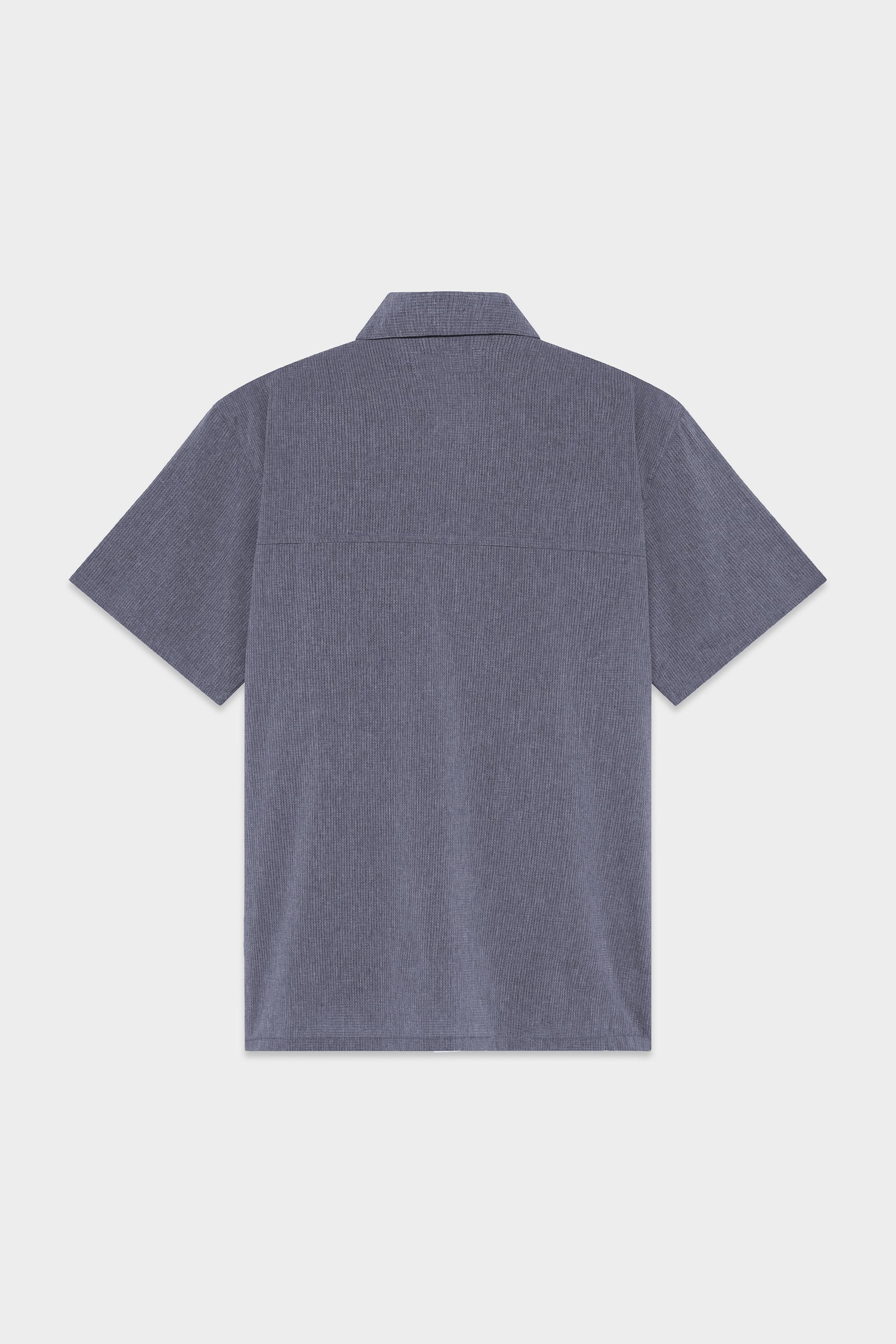 Back view of the 686 Mens Seeker Perforated Button Up by 686, featuring short sleeves, a collar, straight hem, and textured blue fabric. Displayed against a light grey background.