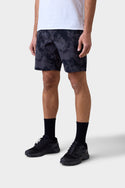A person stands against a plain light background, wearing a white T-shirt, black 686 Mens Everywhere Hybrid Short, black crew socks, and black sneakers. The stylish, stain-resistant hybrid shorts from 686 are breathable. Their face is not visible.