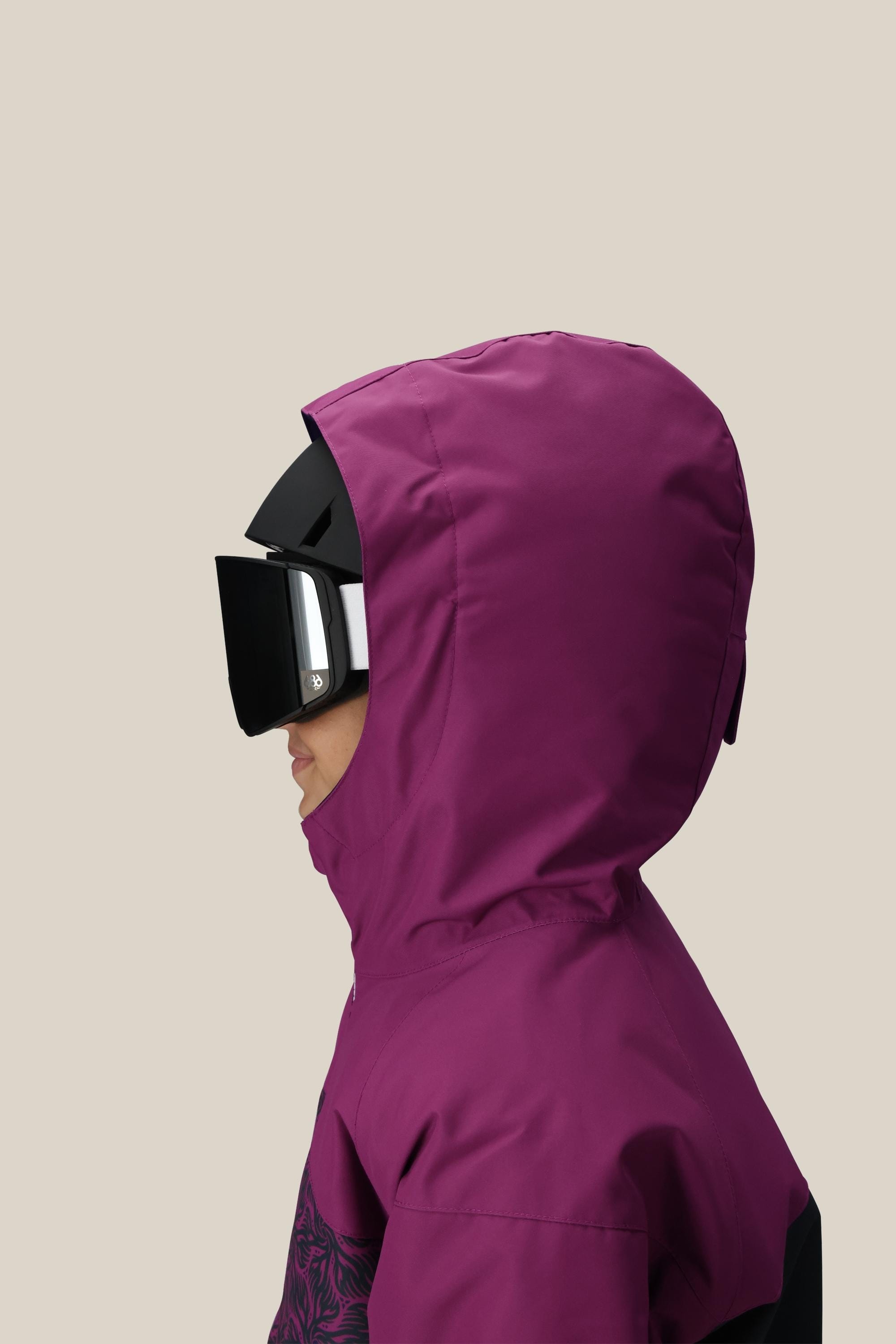 A girl in profile wears the 686 Girls Athena Insulated Jacket with a hood and large black ski goggles, set against a plain beige background.