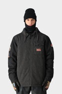 Wearing the 686 x Iron Maiden Mens Insulated Battle Jacket—dark grey with black sleeves, chest pocket, and embroidered patches—a person pairs it with a limited edition black beanie, neck gaiter, and vibrant gloves against a plain light background.