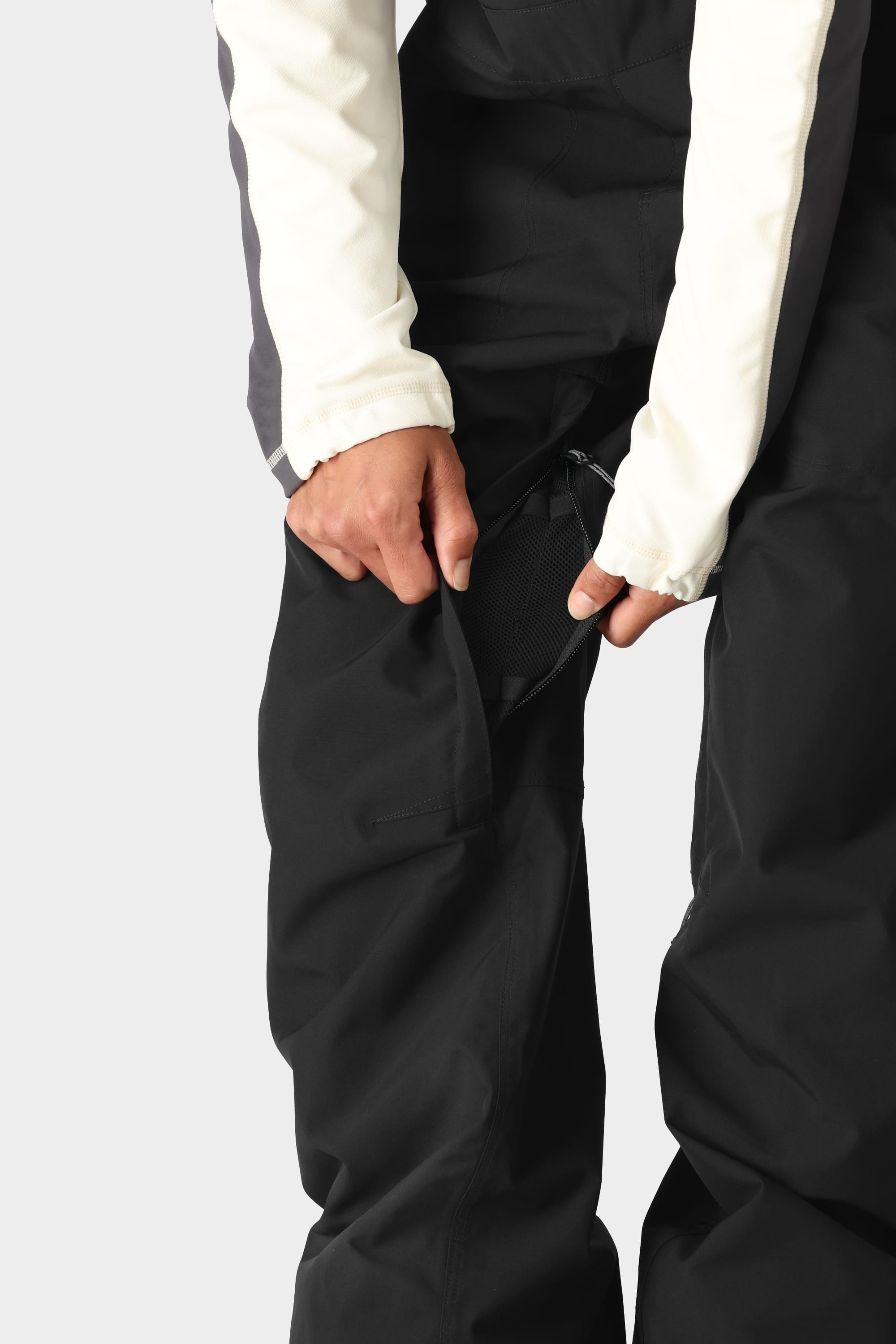 A person wearing the 686 Womens Black Magic 20K Bib unzips a side vent, revealing mesh lining underneath for extra ventilation and insulation.