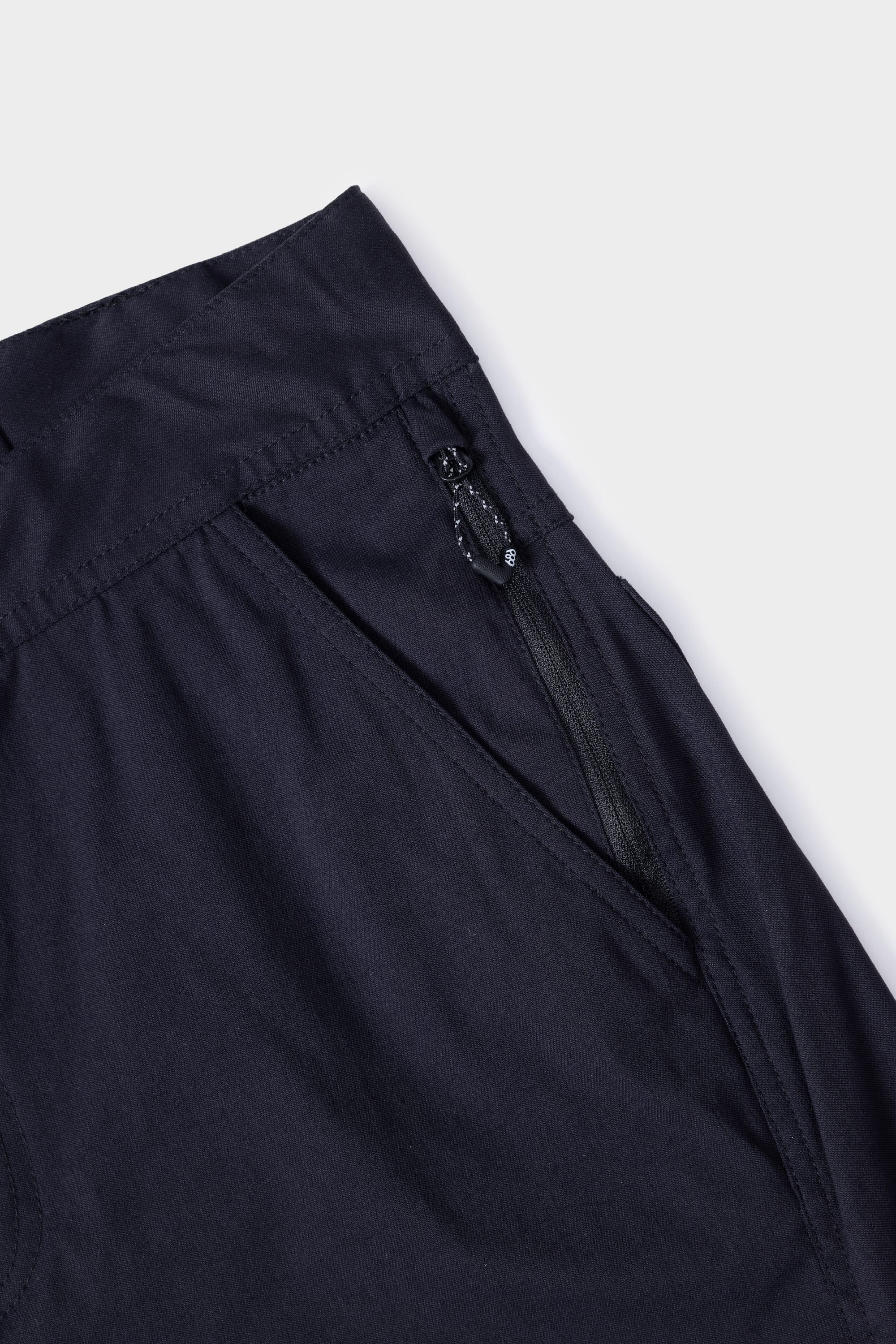 Close-up of the 686 Mens Platform Bike Pant - Relaxed Fit pocket, showing a visible zipper and pull tab. The black fabric appears smooth with detailed stitching, set against a plain white background. Brand: 686.