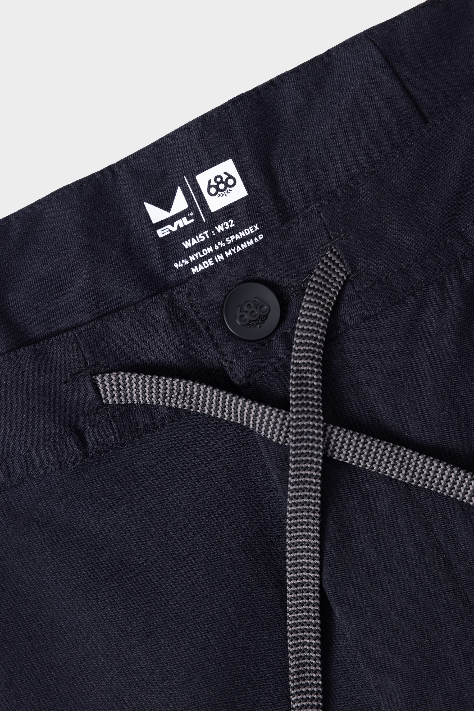 Close-up of the waistband on 686 Mens Platform Bike Pant - Relaxed Fit, featuring a button, drawstring, and inside label with size, material info, and 686 brand logos.