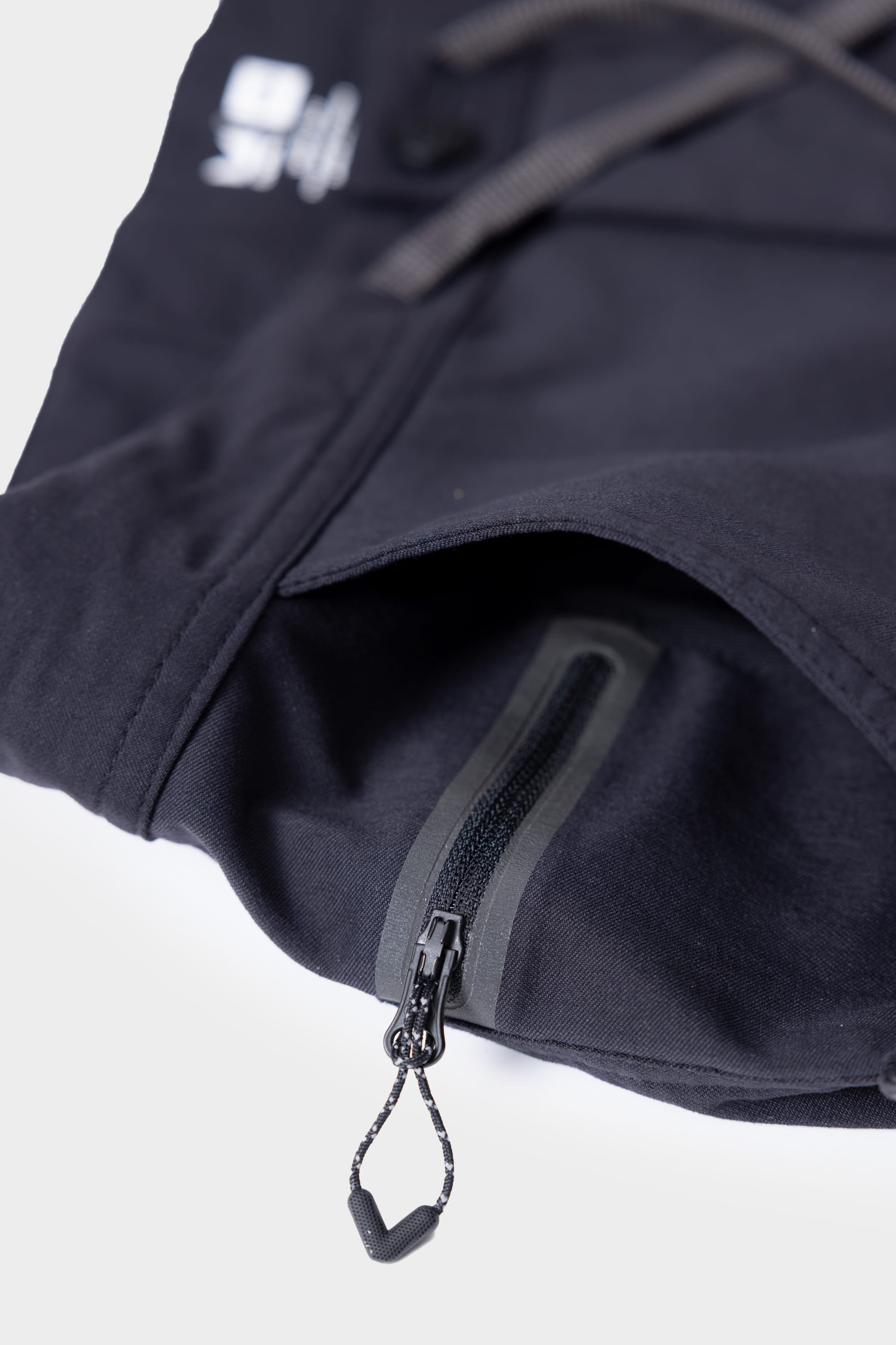 Close-up of the 686 Mens Platform Bike Pant - Relaxed Fit by 686, showing a small waterproof zipper pocket with a black pull tab on black fabric and a drawstring detail in the background.