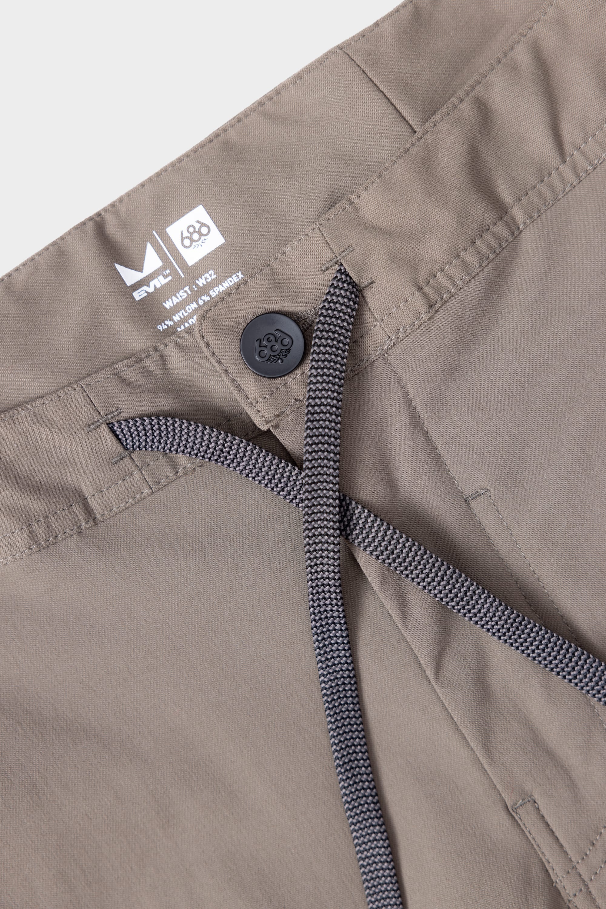 Close-up of 686 Mens Platform Bike Pant - Relaxed Fit waistband shows black button, grey drawstring, and inner tag with 686 branding and size. Durable fabric with detailed stitching around the waistband is visible.