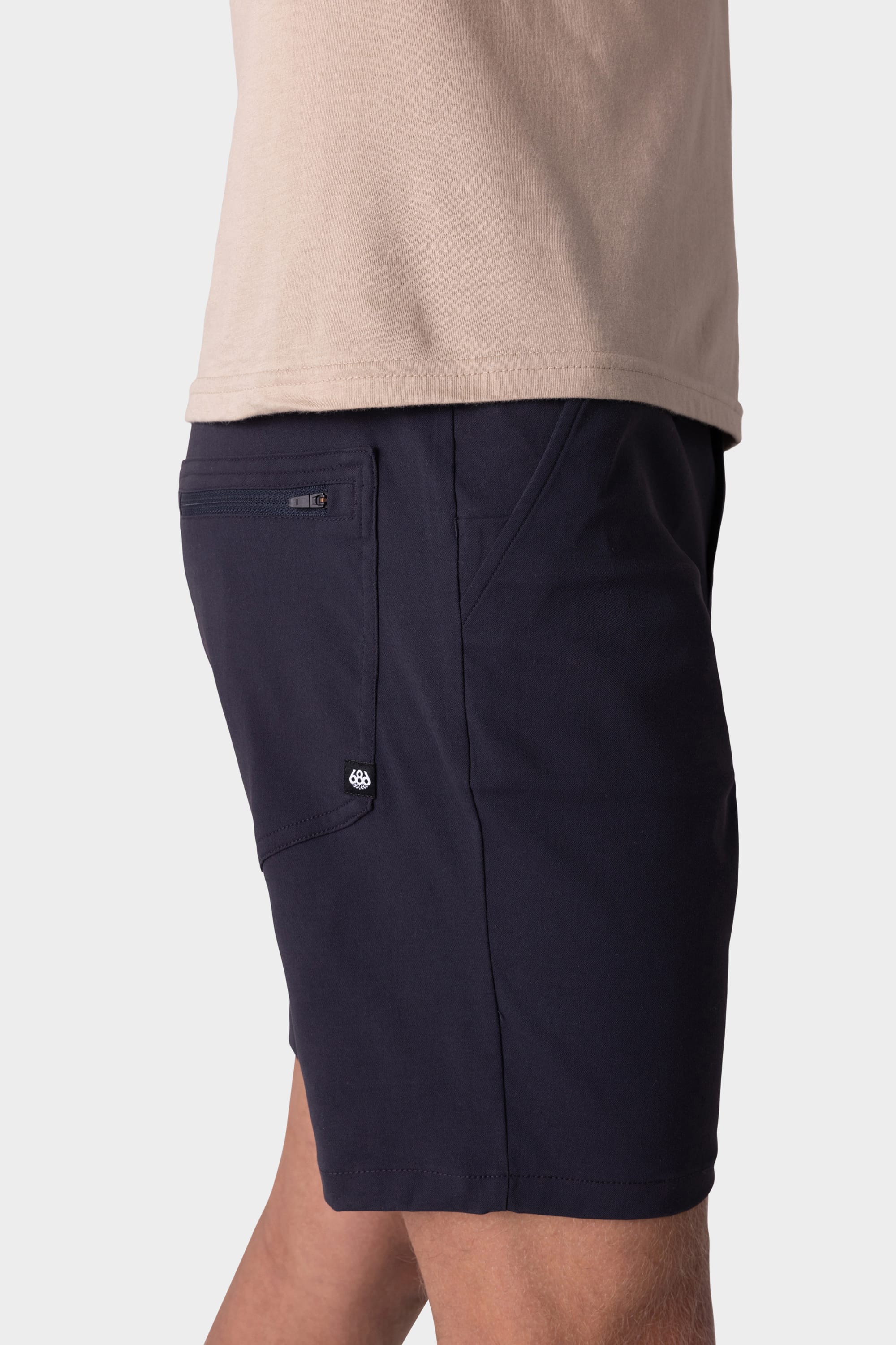 A person wearing 686 Mens Everywhere Hybrid Short in beige and dark navy with a zippered back pocket, shown from the waist down against a plain light background.