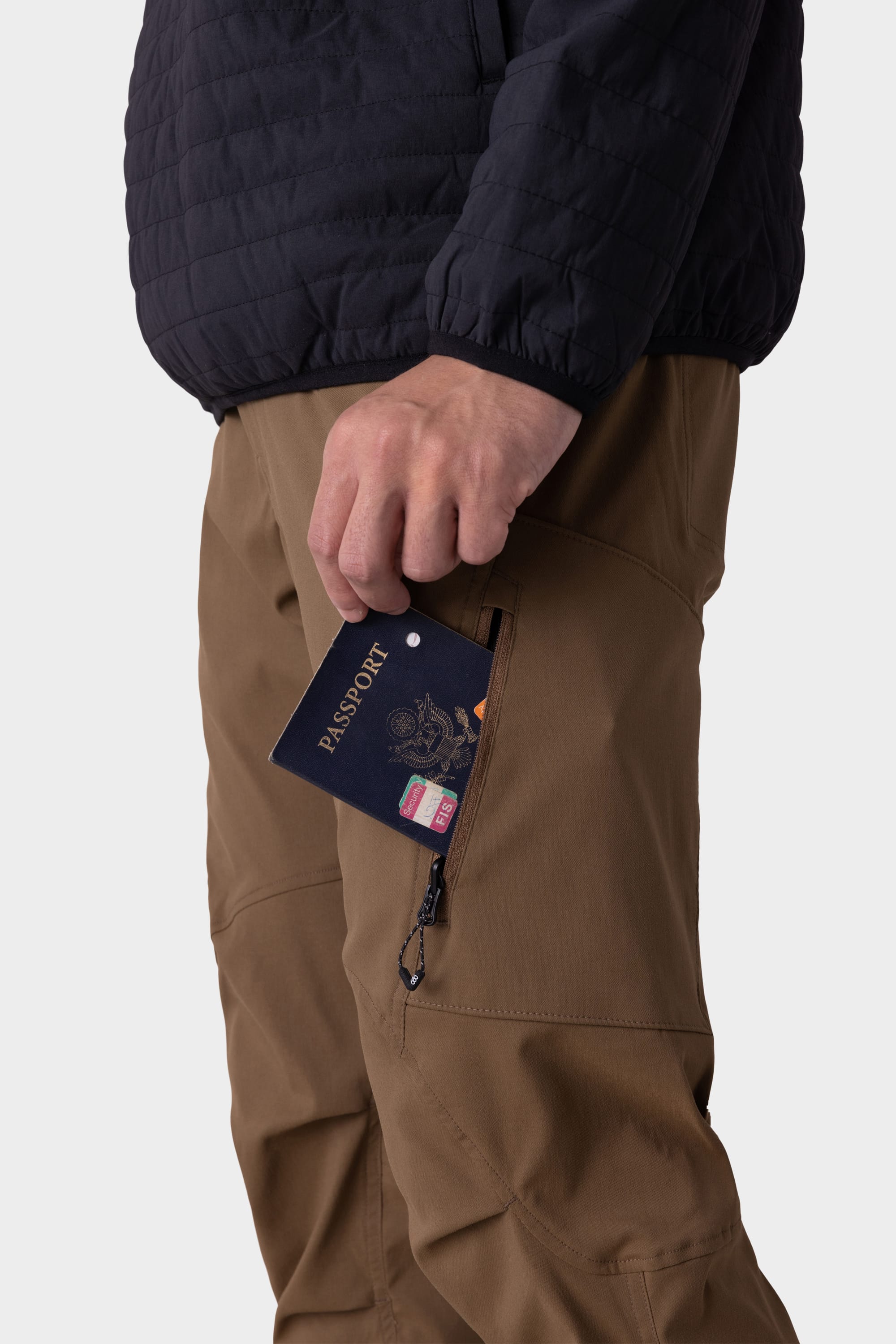 A person in the 686 Mens Anything Cargo Pant - Slim Fit places a passport into a zippered pocket. Only their torso and upper legs are visible, and they’re also wearing a dark jacket.
