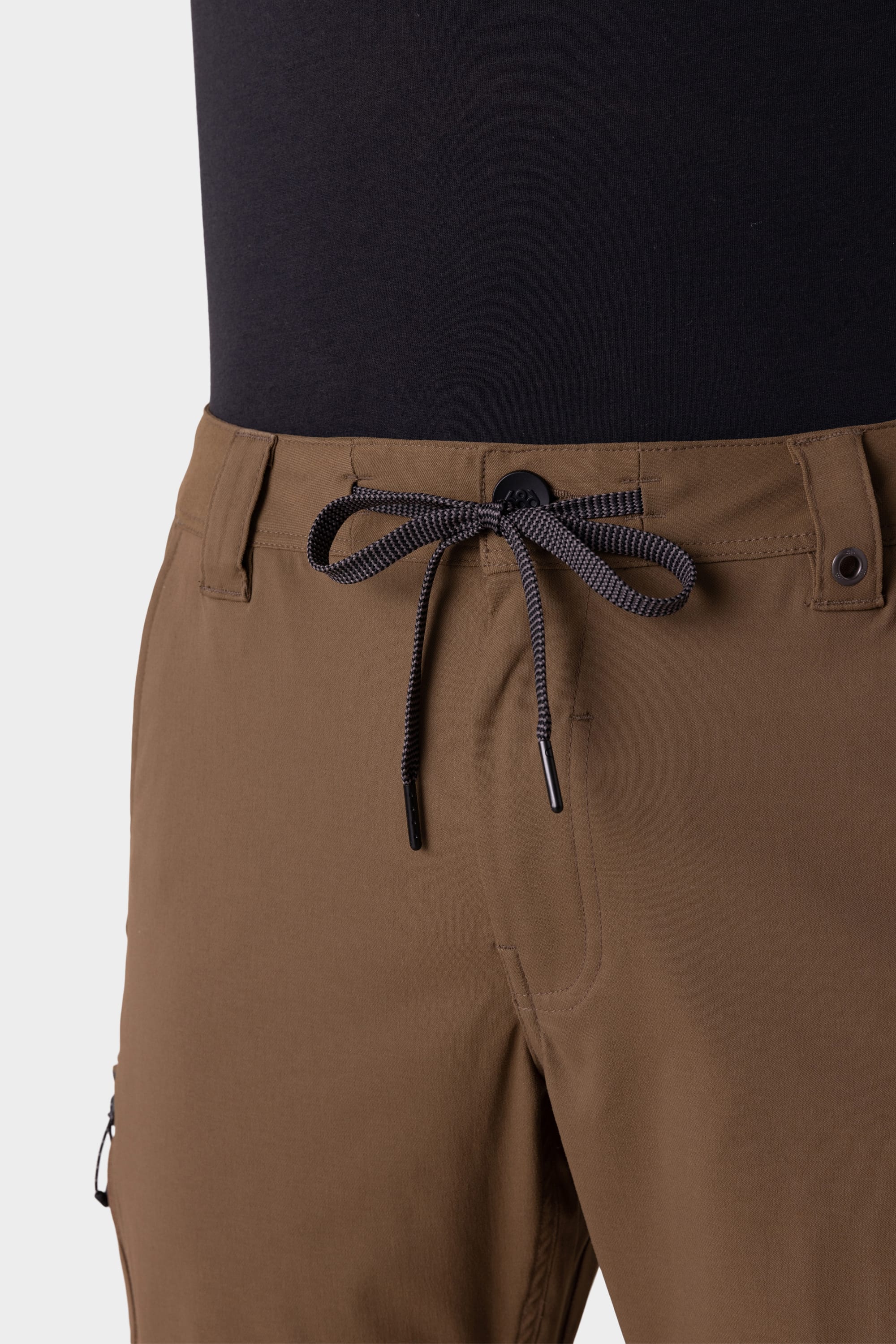 Close-up of a person wearing the 686 Mens Anything Cargo Pant - Slim Fit in brown, featuring breathable fabric, black and white drawstring, button closure, belt loops, a visible zipper pocket, and multiple functional pockets. Paired with a black top.