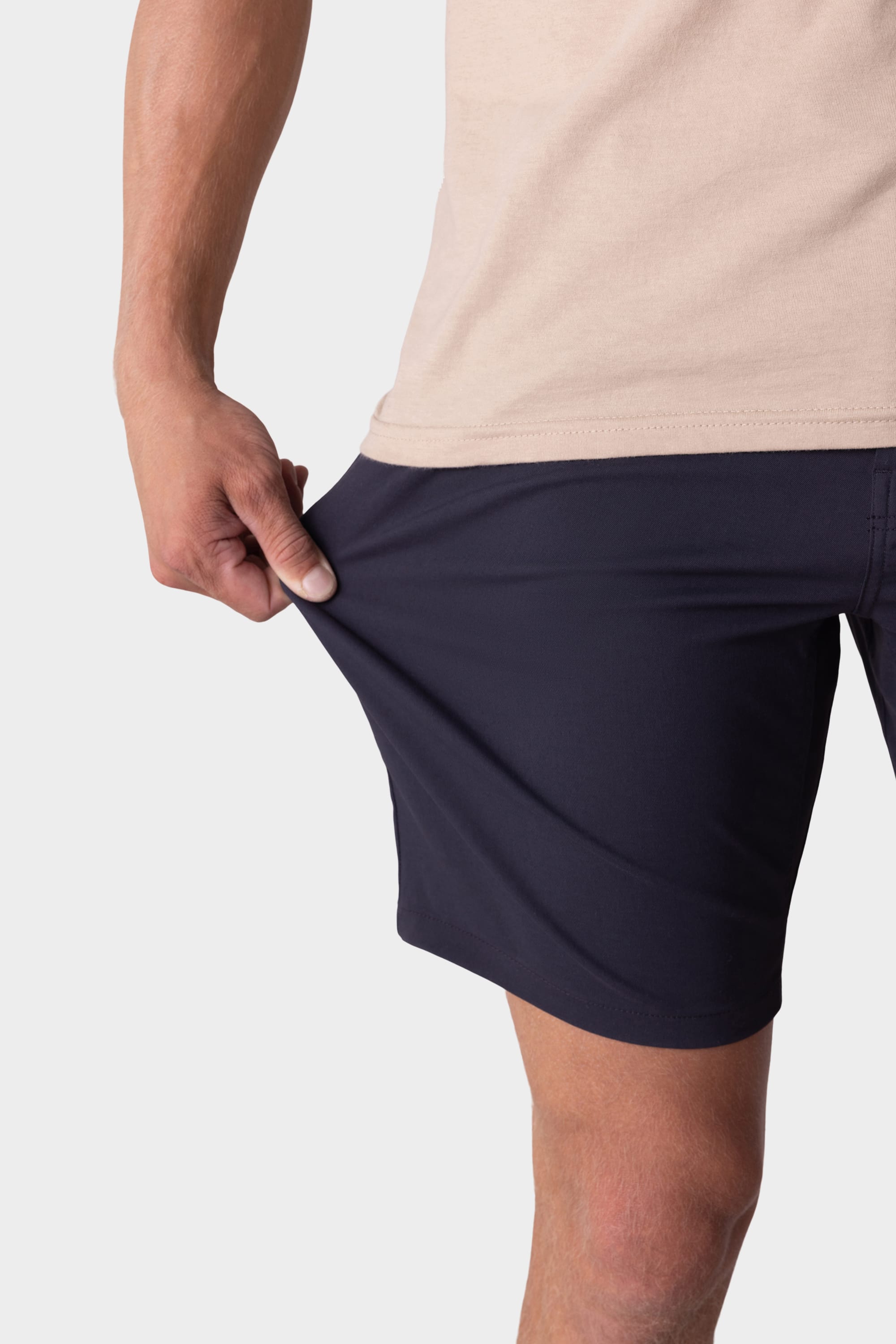 A person in a beige shirt and 686 Mens Everywhere Hybrid Short by 686 stretches the fabric with one hand, showcasing its breathable, flexible material.