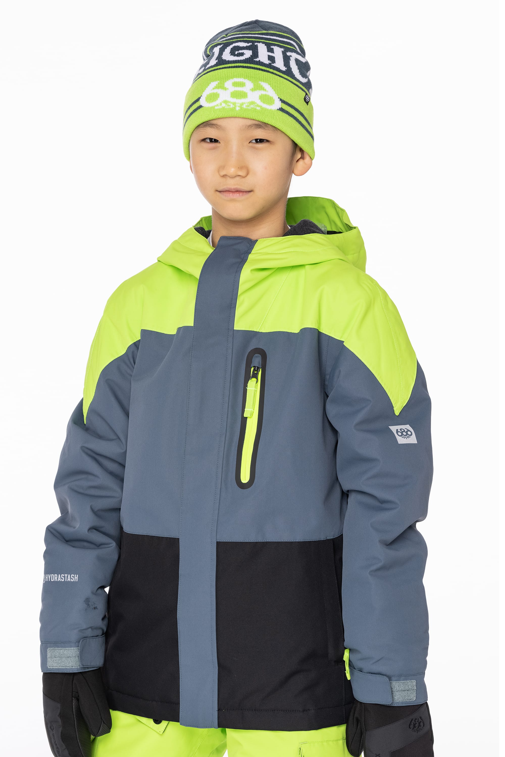 A boy wearing the 686 Boys Hydrastash Insulated Jacket by 686 and a green and gray beanie stands facing the camera with a neutral expression against a plain white background.