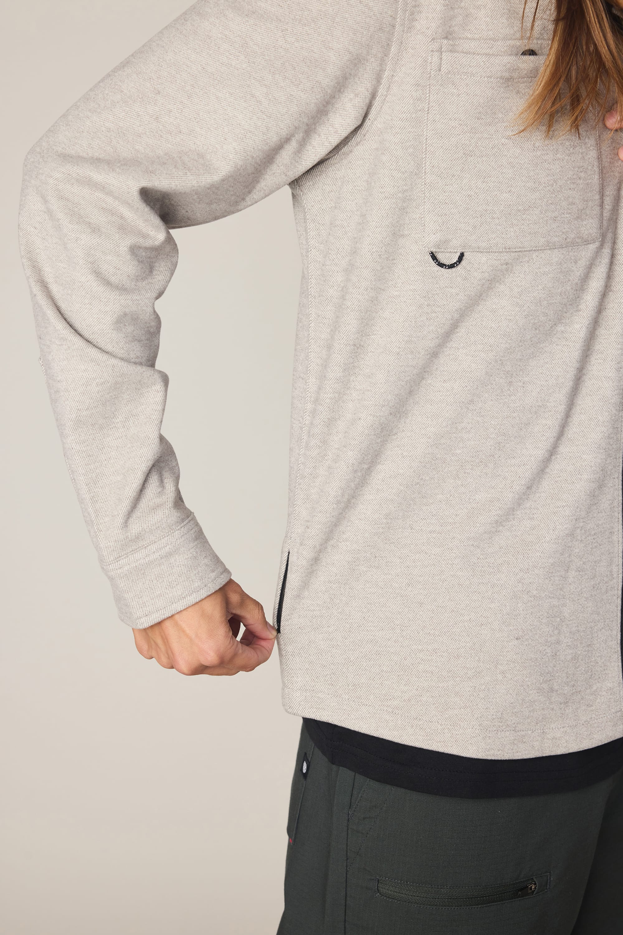 A person wears a light gray 686 Men's Whisper Knit Flannel and dark pants, pulling on a small zipper at the side hem. The person's head is out of frame.