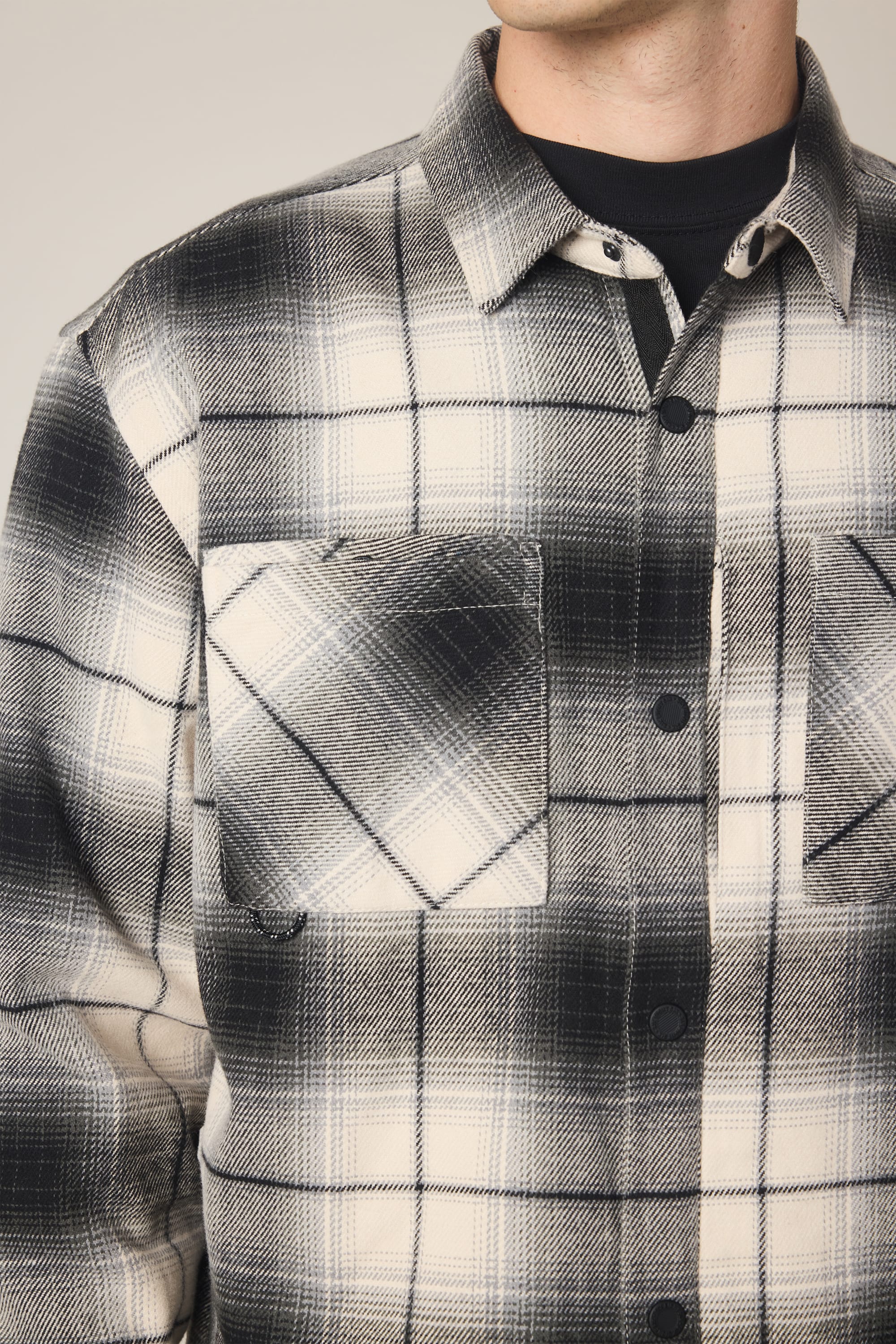 Close-up of a person wearing the 686 Men's Heat Grid Flannel, a black and white plaid polyester shirt by 686 with flap chest pockets and a soft, textured look. The person's head is partially out of frame.