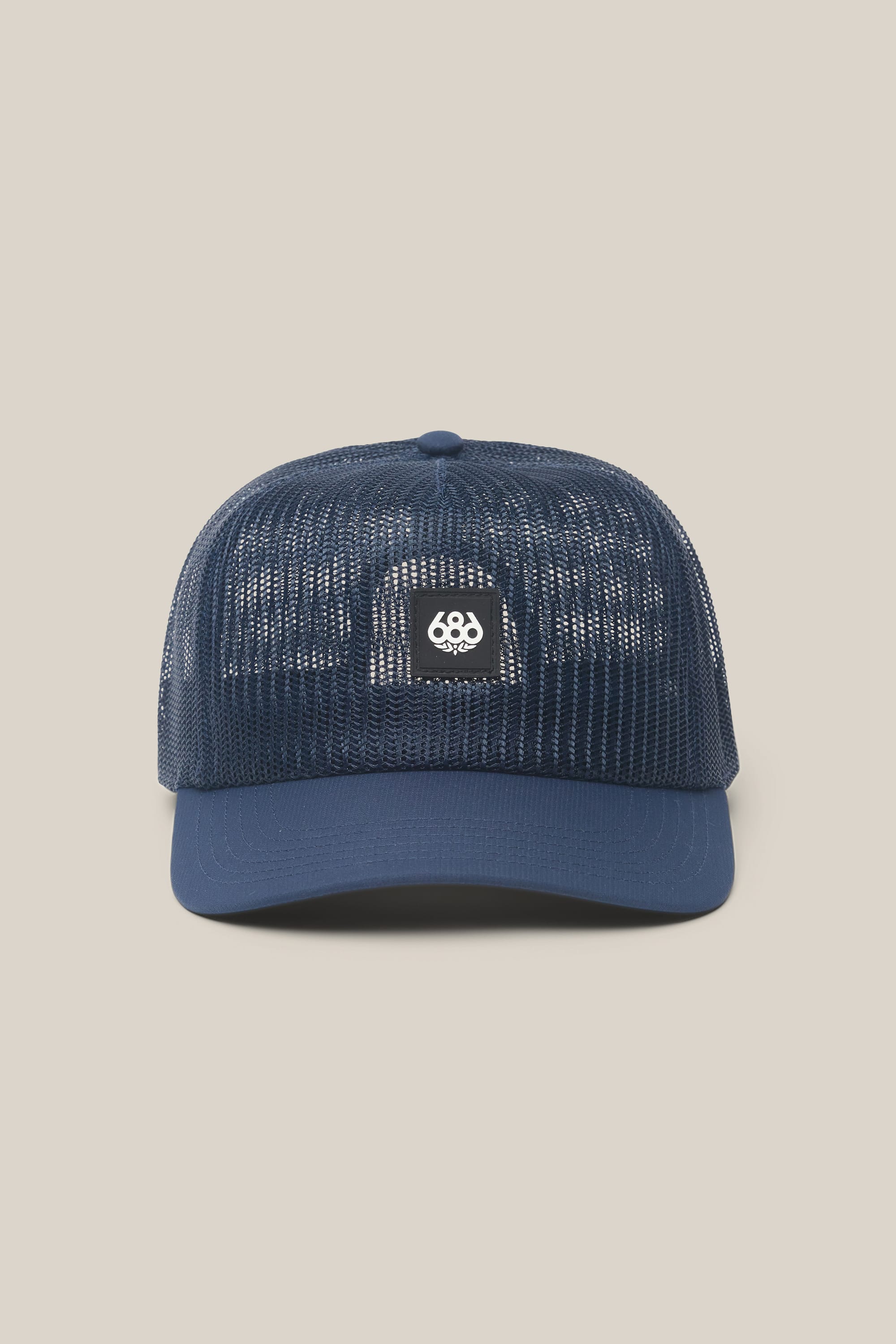 Presenting the 686 High-Pro Knockout Structured 5 Panel Hat by 686—a navy blue mesh trucker cap featuring a curved brim and a small rectangular black patch on the front with a white 686 logo. This stylish men’s hat boasts a breathable design, making it ideal for daily wear. The product is displayed against a plain light beige background.