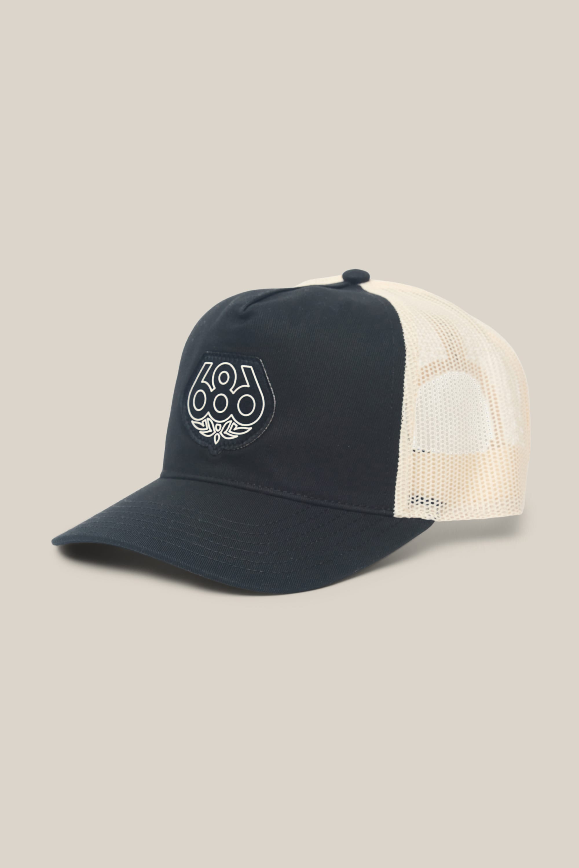 The 686 Mid-Pro Wreath Unstructured 5 Panel Mesh Hat by 686 is a navy blue and white men's hat with a mesh back and a white embroidered geometric logo on the front, shown against a neutral beige background.