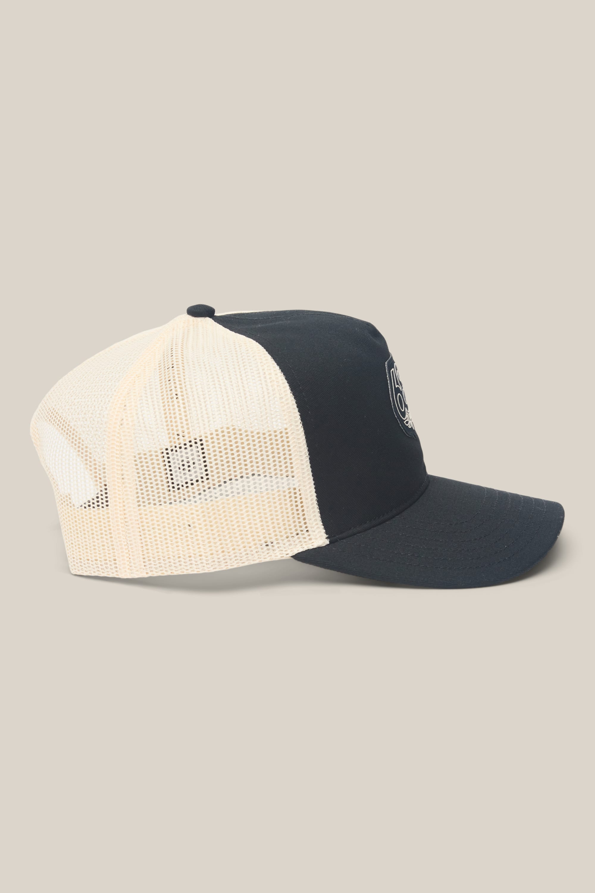 The 686 Mid-Pro Wreath Unstructured 5 Panel Mesh Hat by 686 is a black and white trucker hat with a curved bill, black front panel, and small round embroidered logo‚Äîcrafted from durable polyester cotton. Shown in profile on beige background.