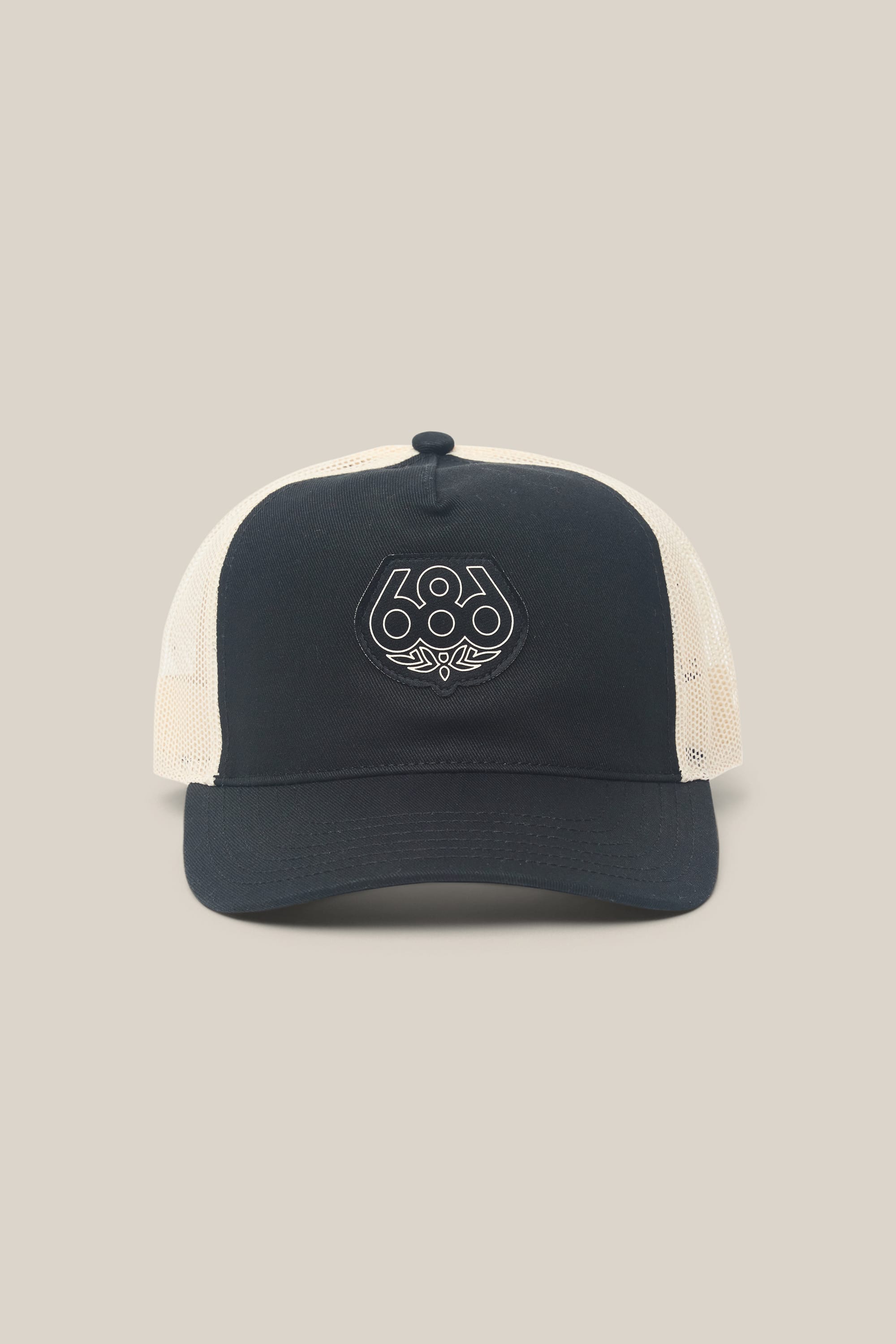 The 686 Mid-Pro Wreath Unstructured 5 Panel Mesh Hat by 686 is a men's black and white trucker hat featuring an embroidered 686 logo on the front, a breathable mesh back, and is made from durable polyester-cotton woven fabric, shown against a plain beige background.