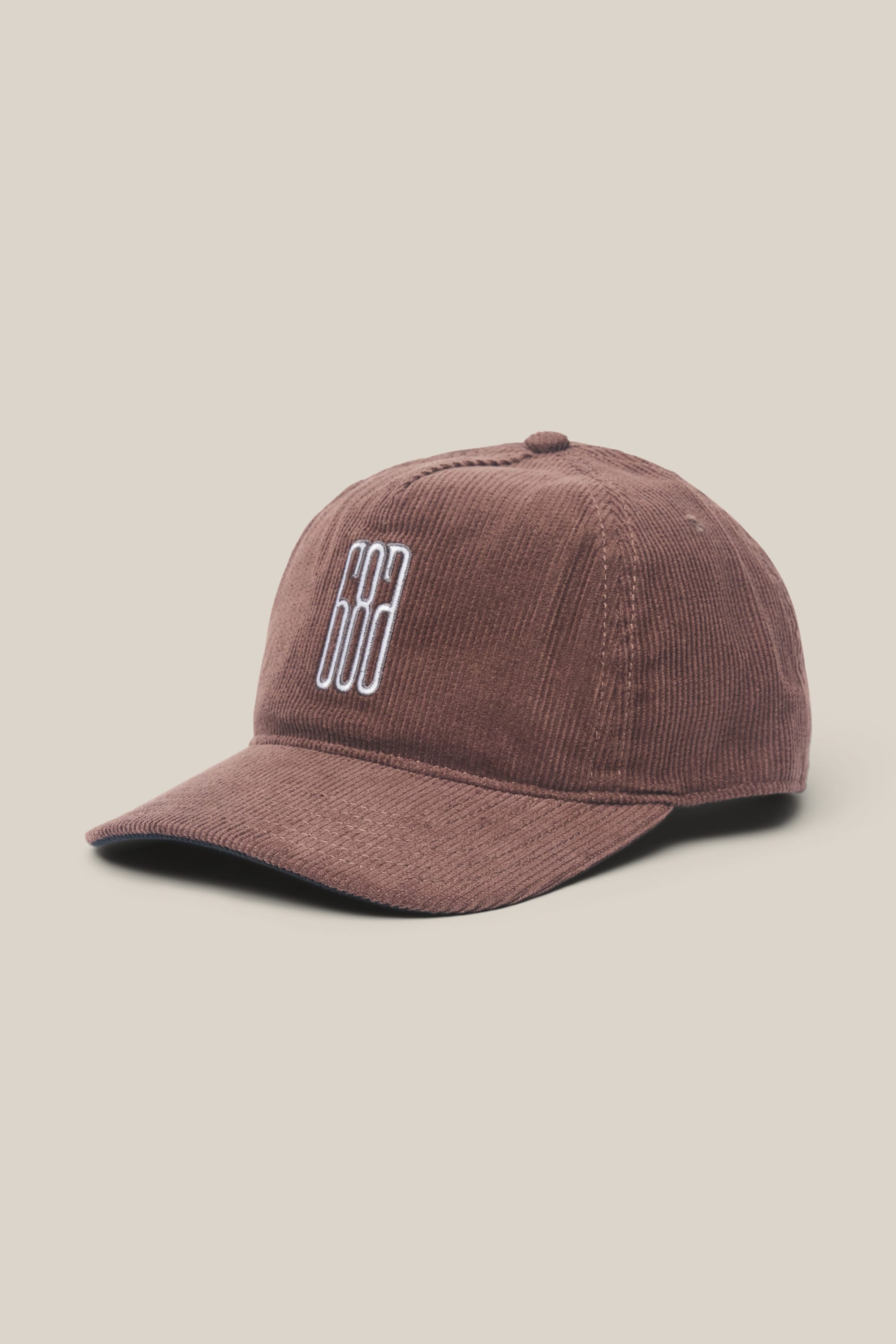 The 686 Mid-Pro Ghost Cord Unstructured 5 Panel Hat by 686 is a brown corduroy baseball cap featuring a curved brim and white geometric embroidery, shown on a light beige background.