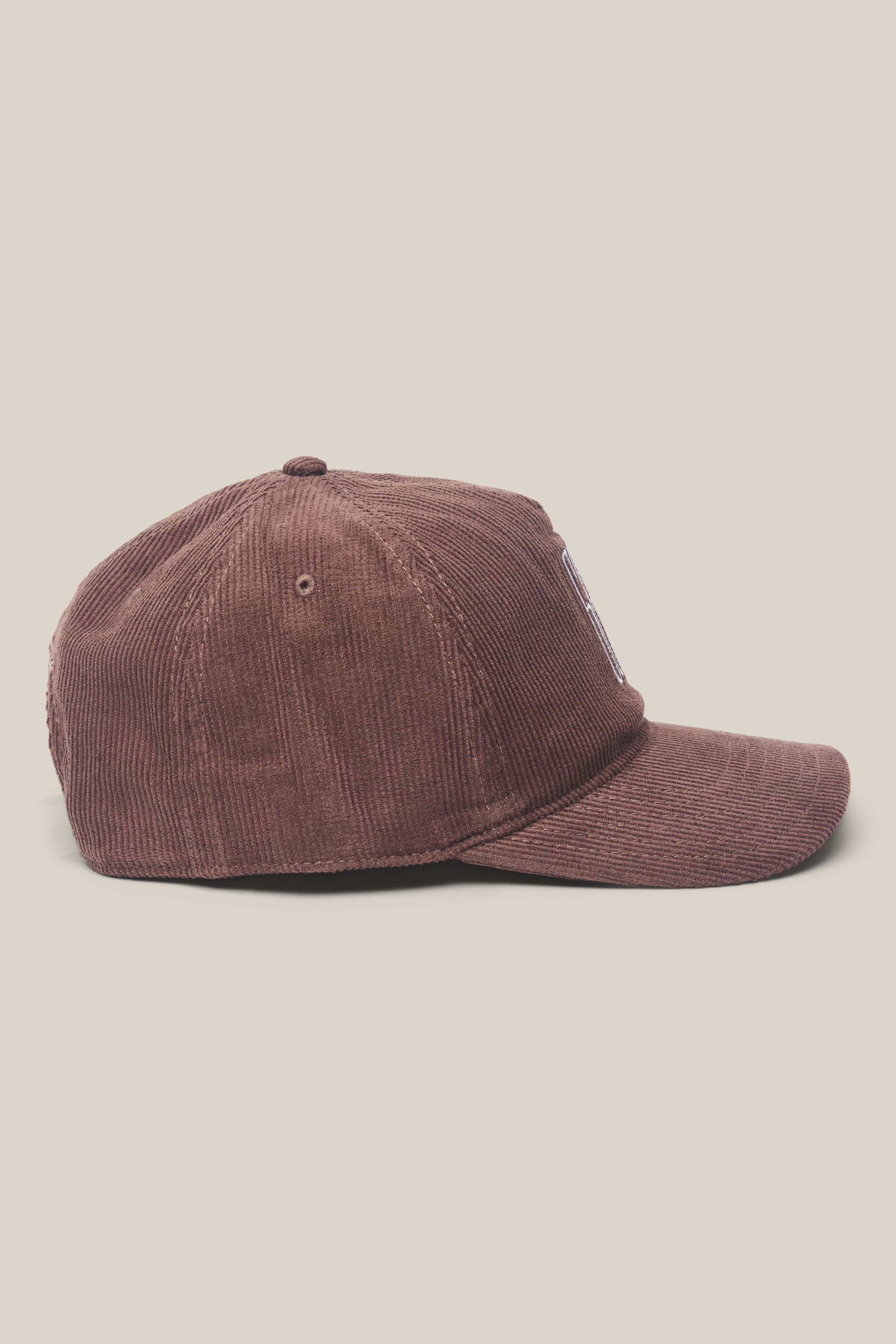 Side view of the 686 Mid-Pro Ghost Cord Unstructured 5 Panel Hat by 686, a brown corduroy men's hat with a curved brim and visible stitching, shown against a plain light beige background.