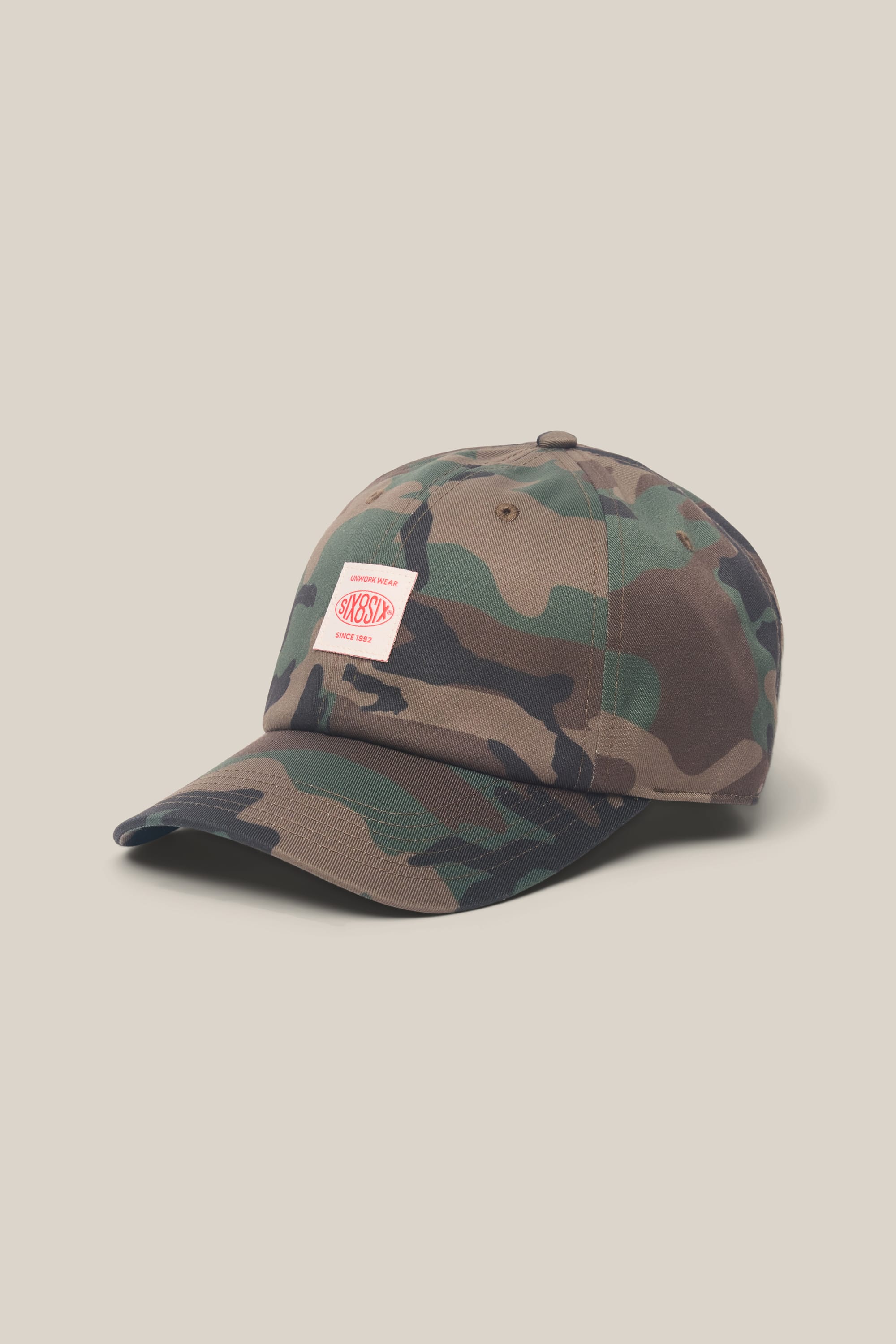 The 686 Low-Pro Unwork Unstructured 6 Panel Hat by 686 is a men's polyester-cotton cap with a camouflage pattern and a white rectangular patch with red text on the front, shown on a plain beige background.
