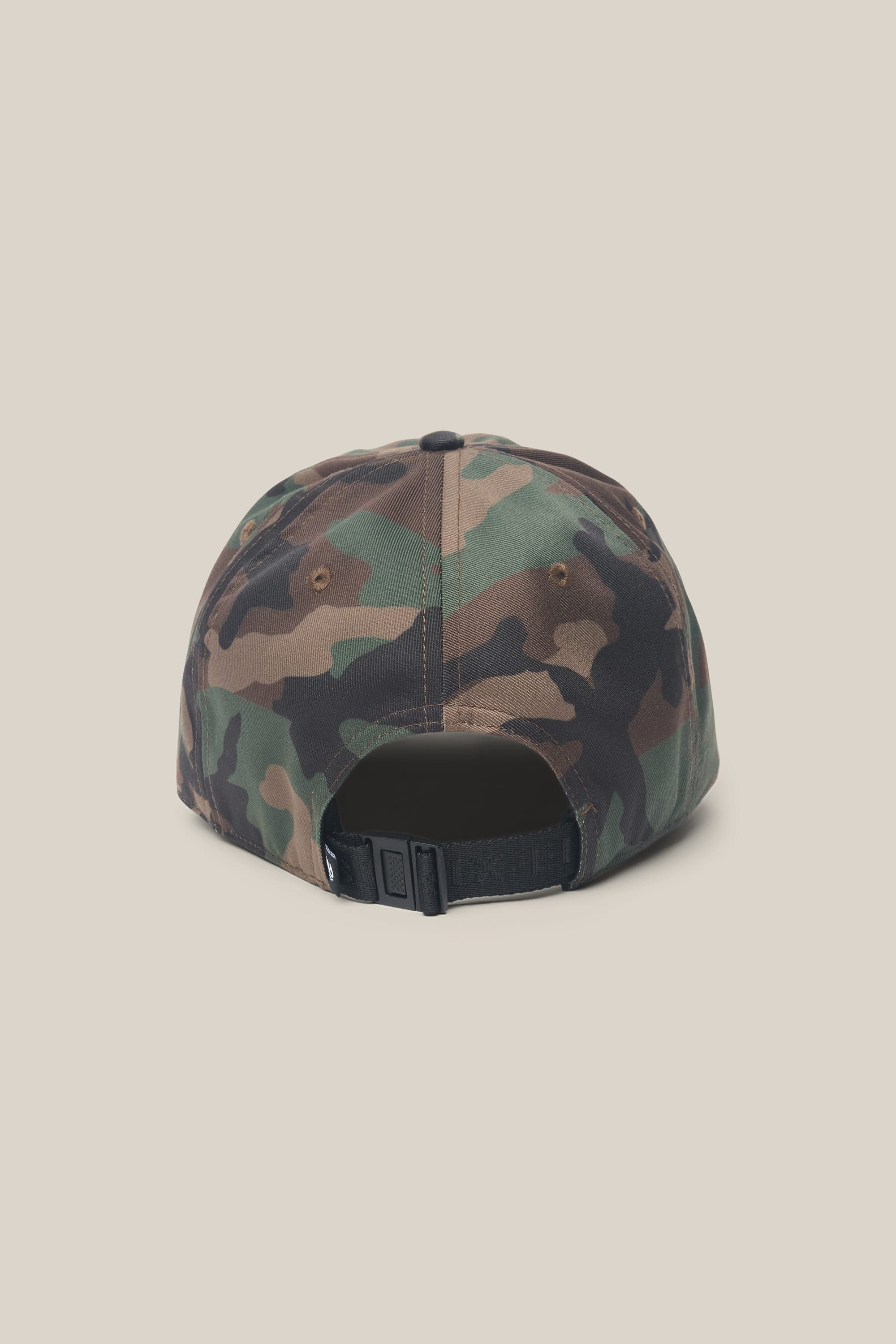 The 686 Low-Pro Unwork Unstructured 6 Panel Hat by 686 is shown from the back in green and brown camouflage, featuring a black adjustable strap and a small opening above it, set against a plain light beige background.