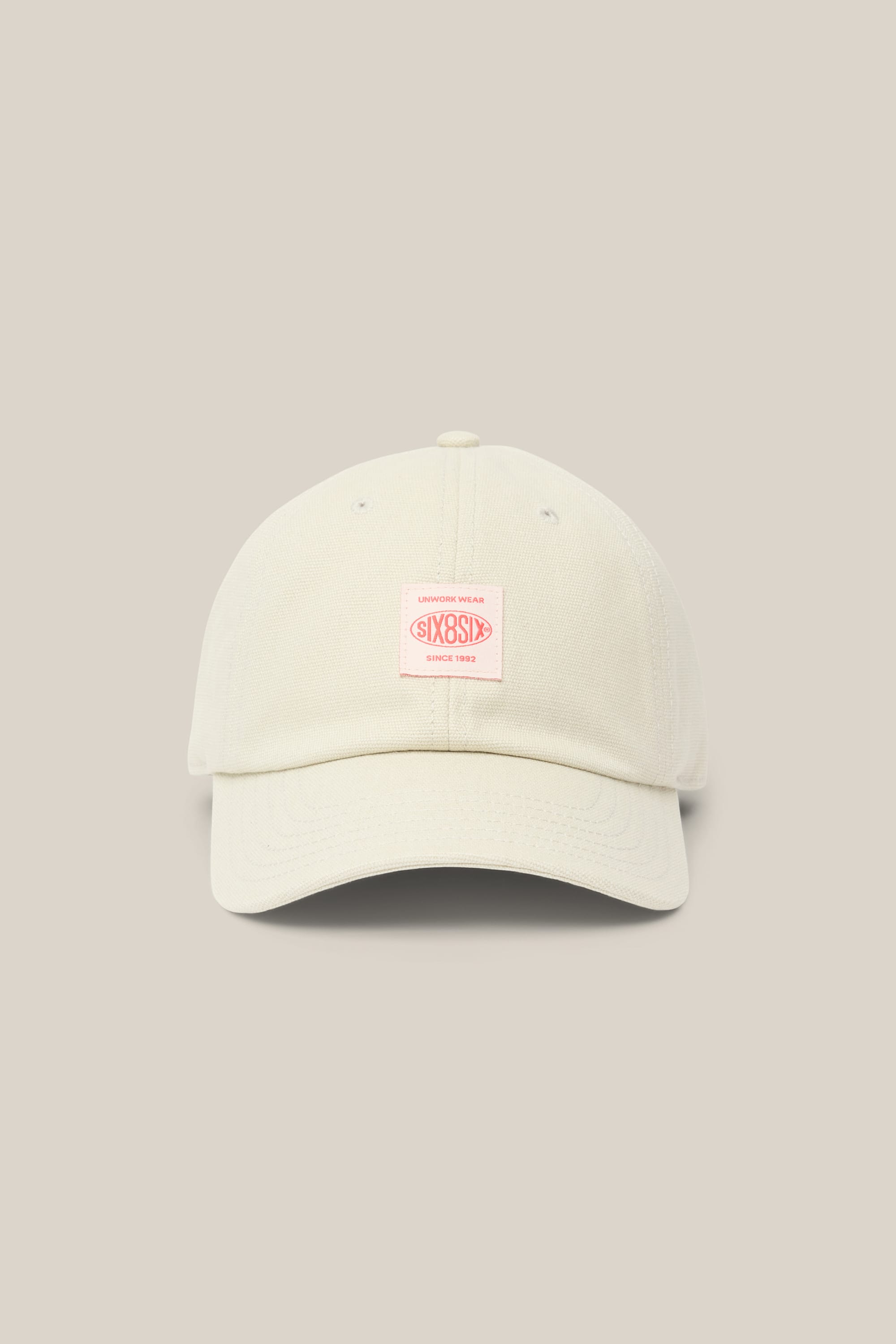 The 686 Low-Pro Unwork Unstructured 6 Panel Hat by 686 is a light beige polyester-cotton cap with a curved brim and a pink rectangular text patch on the front, shown against a plain beige background.