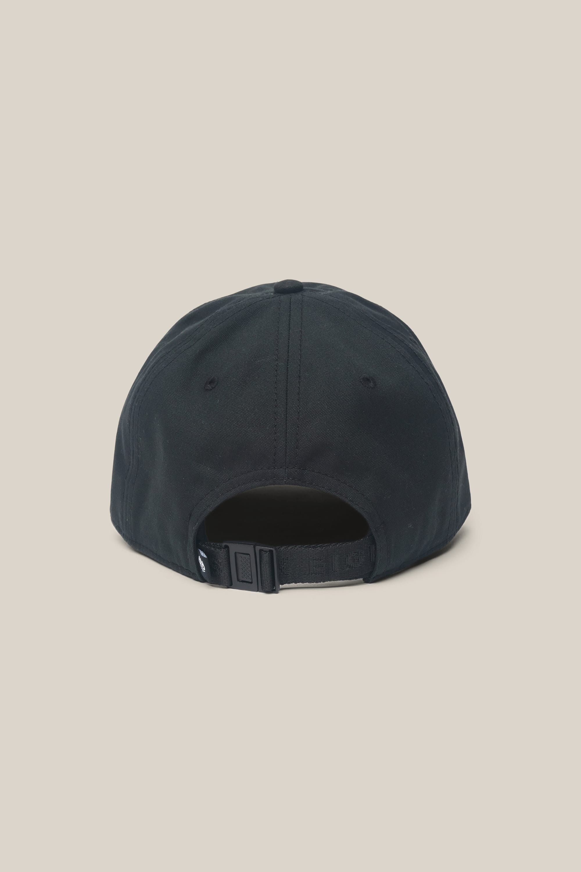 The 686 Low-Pro Unwork Unstructured 6 Panel Hat by 686 is shown from the back, highlighting its adjustable strap with a plastic buckle, set against a plain beige background. This classic black men's baseball cap is crafted from a durable polyester-cotton blend for all-day comfort and style.