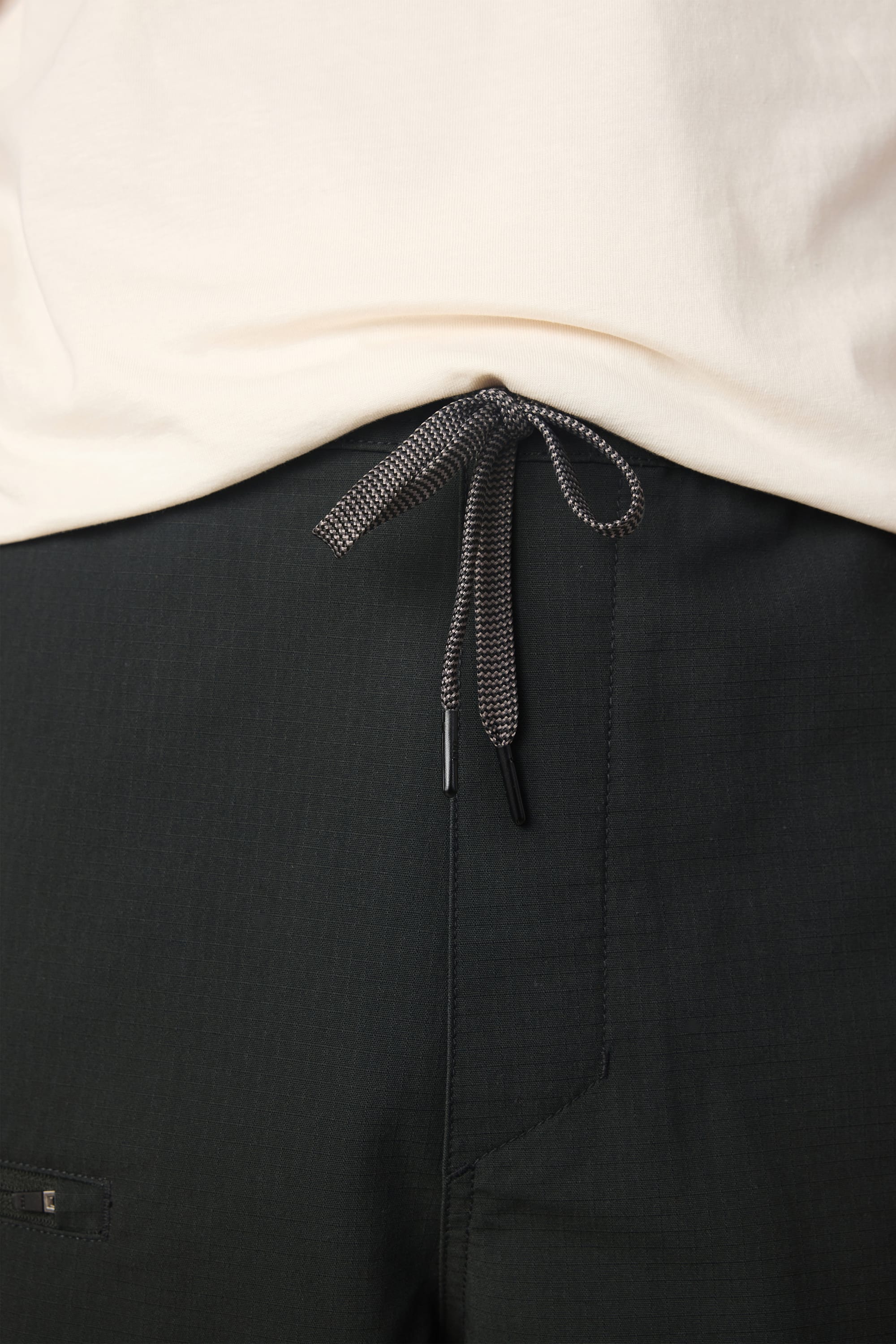 Close-up of a person wearing a white shirt tucked into the 686 Men's Free Loader Pant - Loose Fit in black, featuring a black and white drawstring tied in a bow at the waistband.