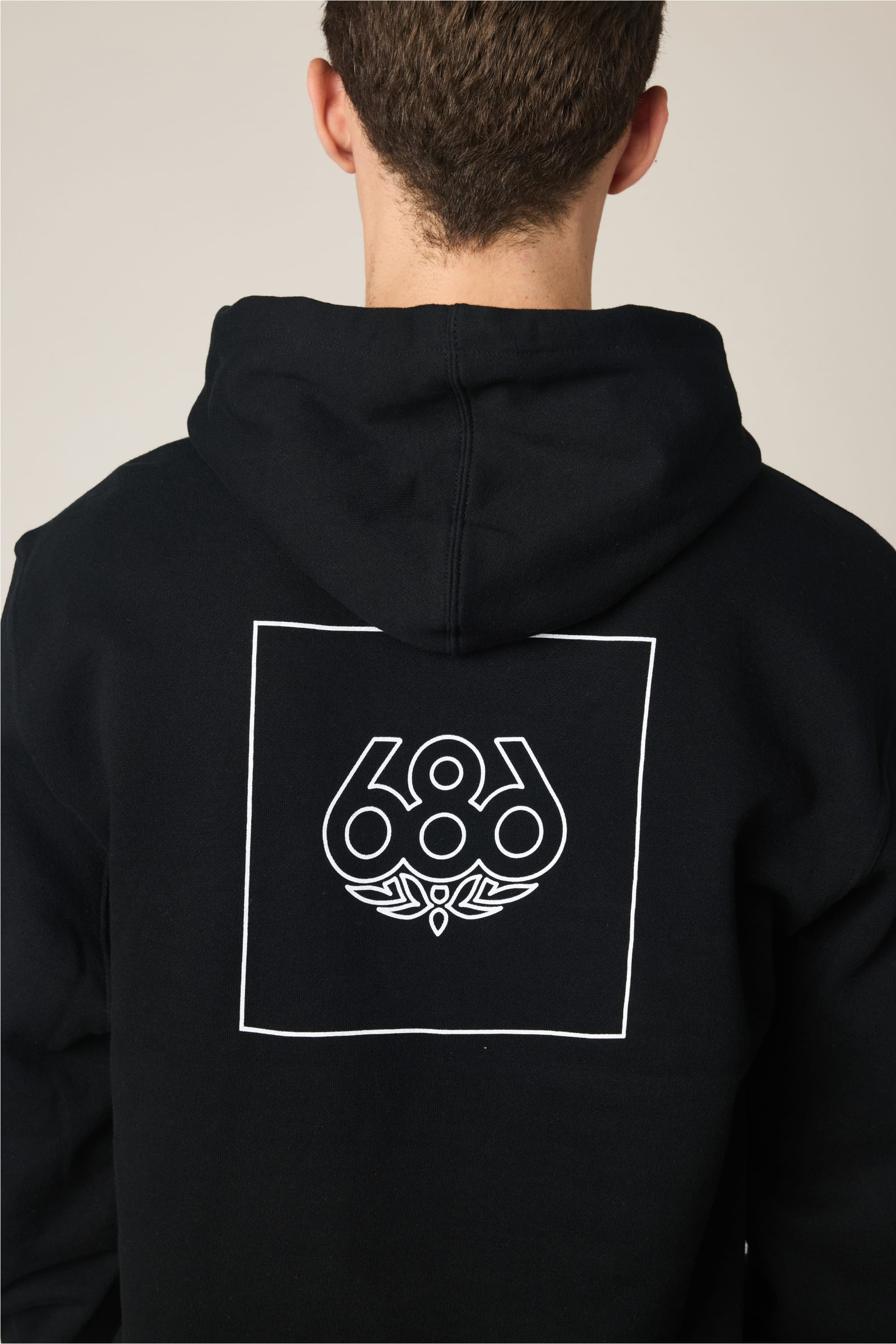A person seen from behind wears the 686 Wordmark Athletic LS Hoody by 686‚Äîa men's cotton sweatshirt with a black hood, featuring a white outlined square and stylized ‚Äú686‚Äù logo on the back.