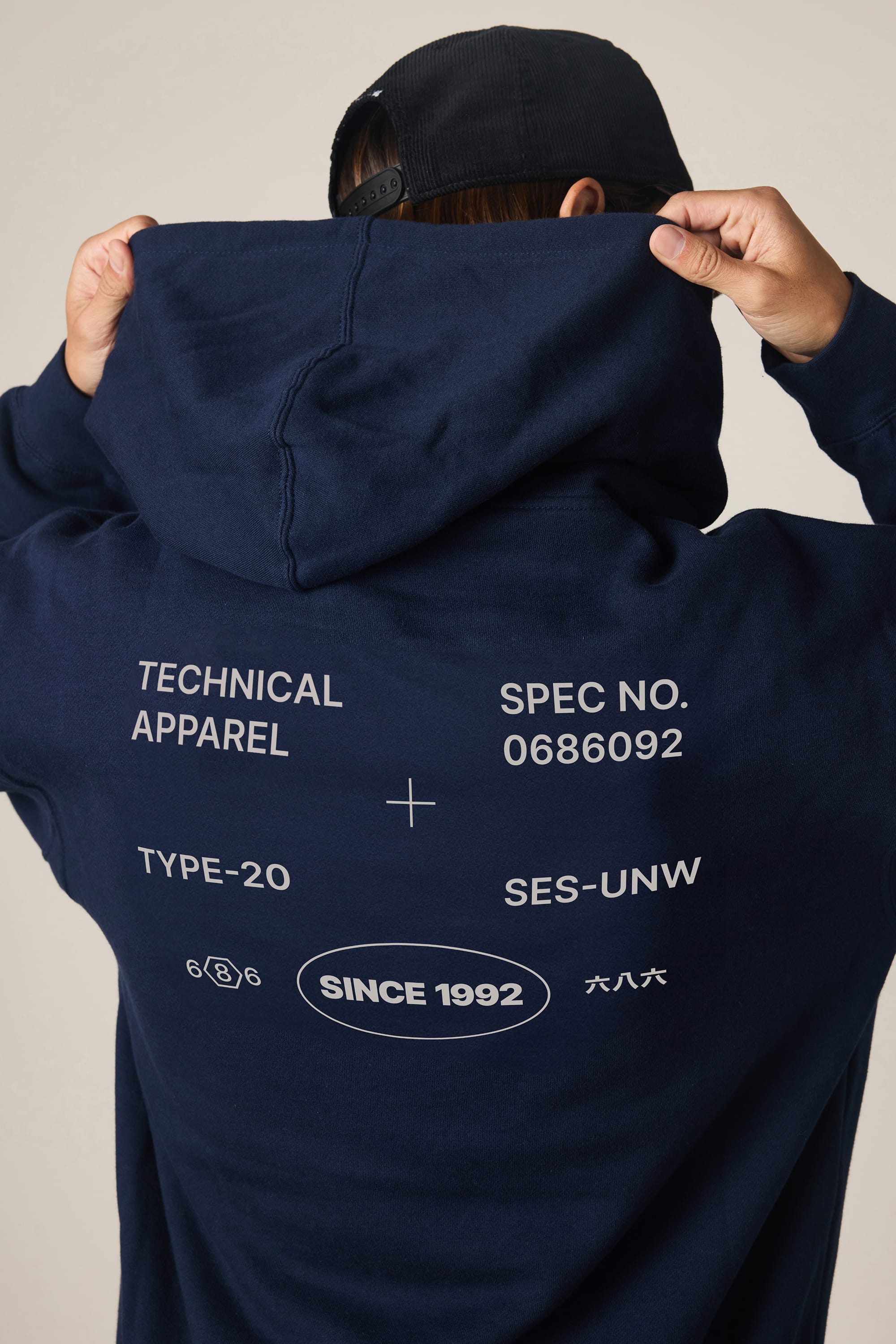A person wearing the 686 Men's Unwork Spec Athletic LS Hoody in navy blue lifts the hood, showing white text and numbers like “TECHNICAL APPAREL,” “SINCE 1992,” plus various codes and symbols on the back. Brand: 686.