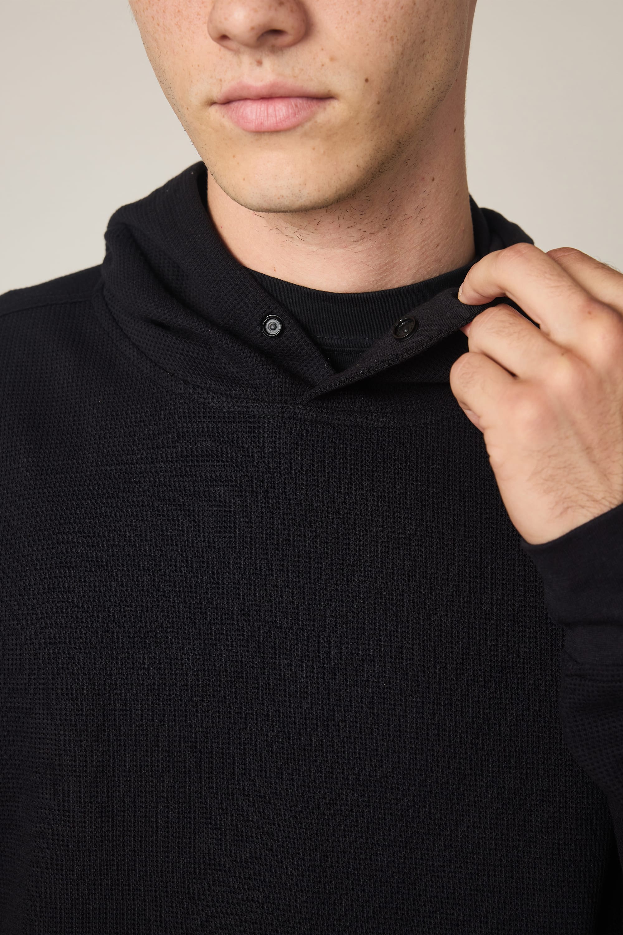 A person wearing the 686 Men's Let's Chill Waffle Hoody in black is holding the collar with one hand, showing only their lower face and upper torso.