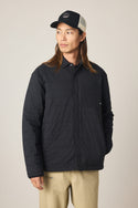 A person in the 686 Men's Thermaldry Insulated Shacket, beige pants, and a black-and-white baseball cap stands with one hand in their pocket, looking to the side against a plain light background.