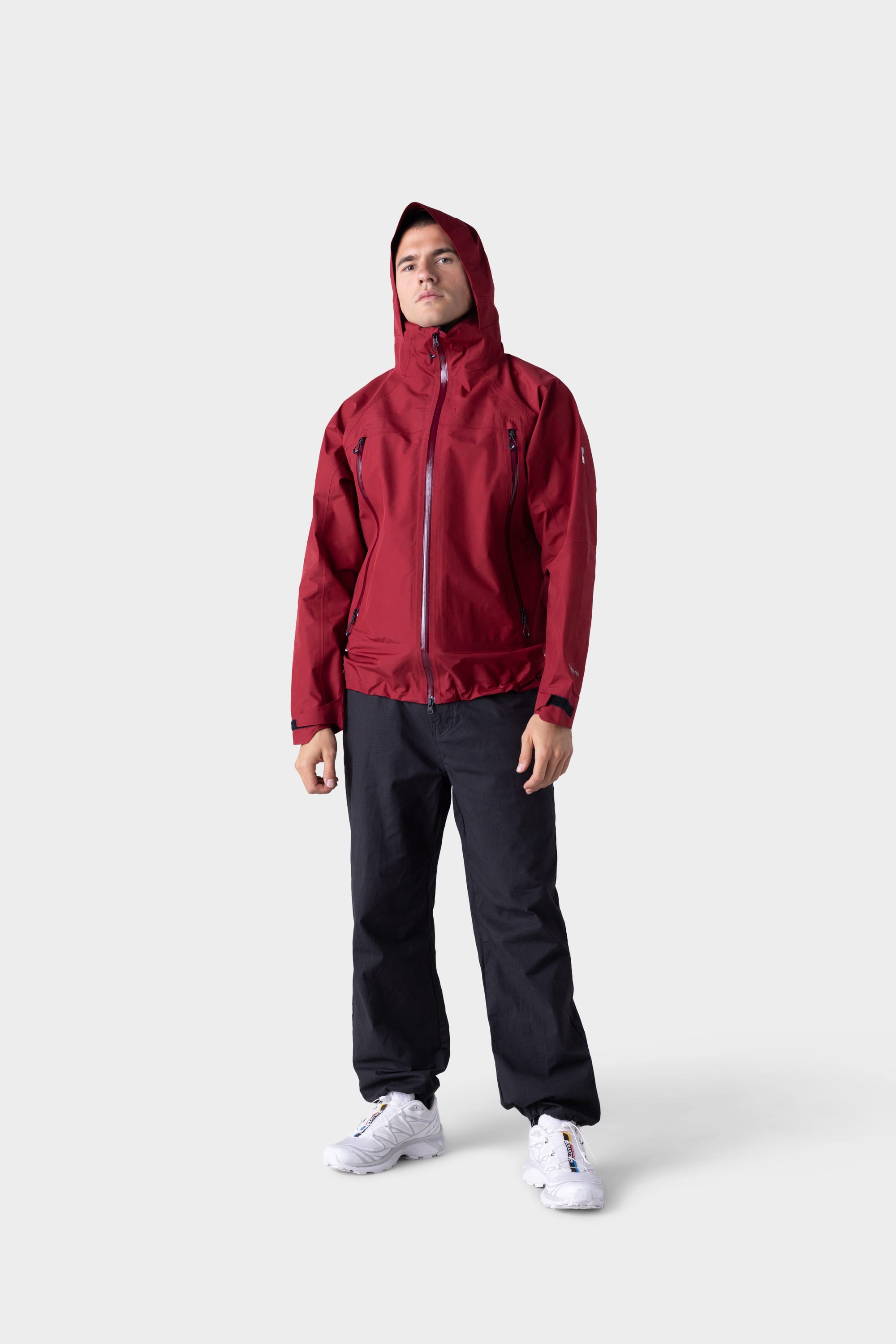 A person stands facing forward, wearing the 686 Mens GORE-TEX PACLITE® Jacket, black pants, and white sneakers against a plain light gray background.