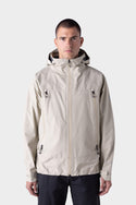 A person wearing the 686 Mens GORE-TEX PACLITE® Jacket in light beige with zippered chest pockets and black pants stands against a plain light gray background.