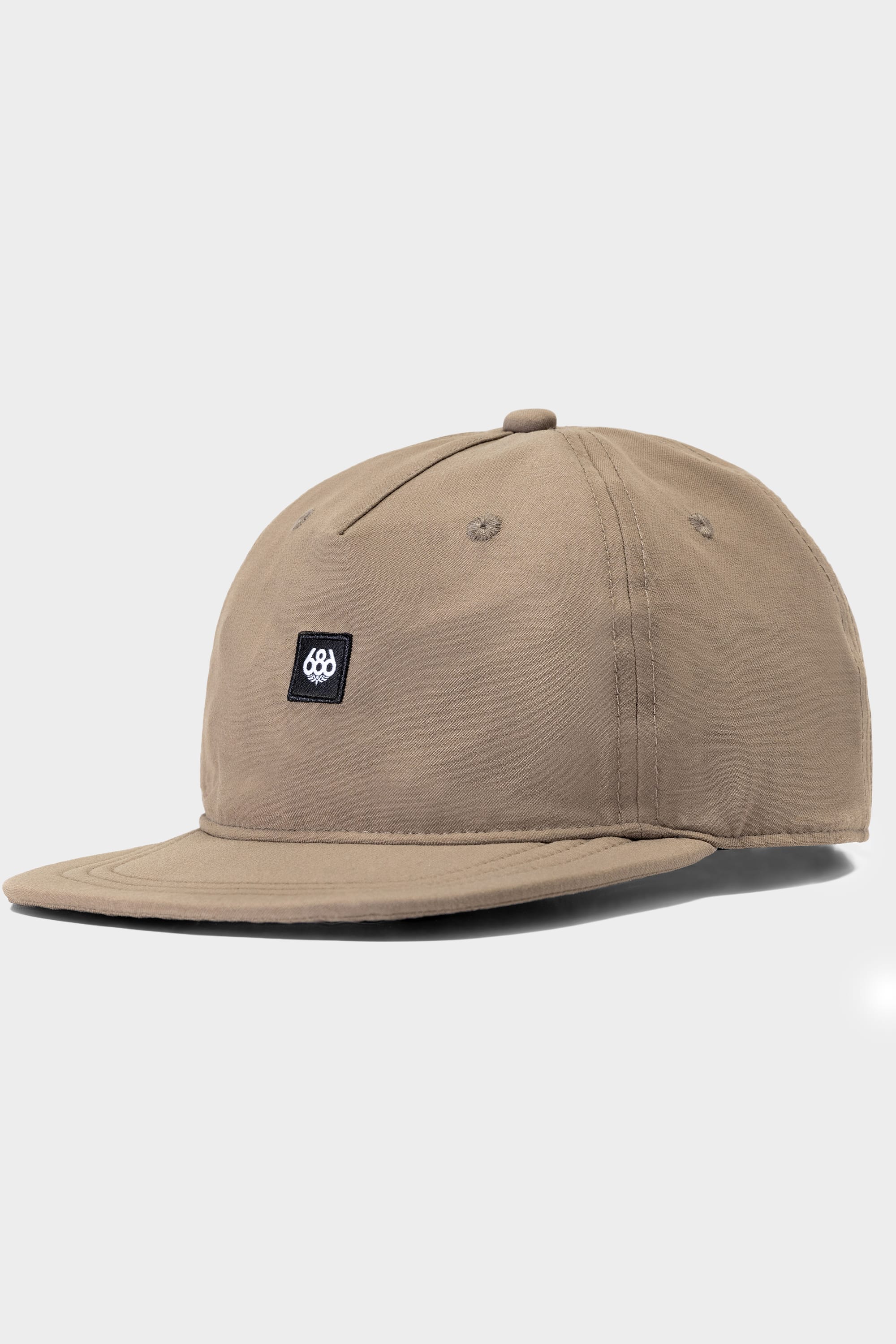 The 686 Packable Everywhere Hat by 686 is a tan baseball cap with a curved brim and a small black rectangular patch with a white circular logo on the front, shown against a plain light gray background.