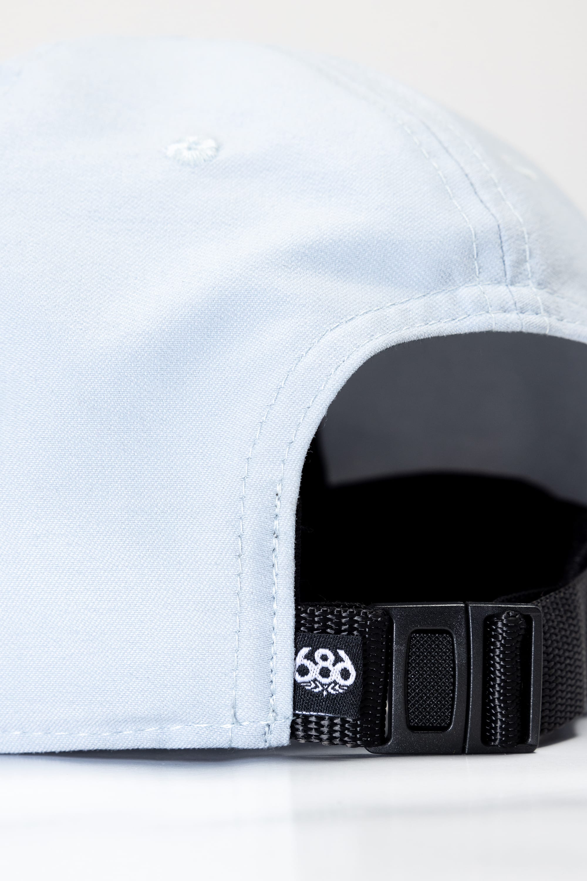 Close-up of the back of the 686 Packable Everywhere Hat by 686 in light blue, featuring a black adjustable strap and a small embroidered white logo near the strap opening.