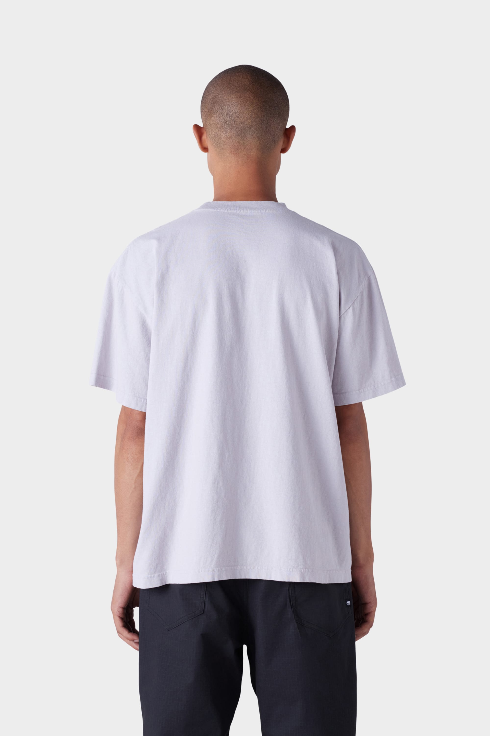 A person with a shaved head is shown from behind, wearing the 686 Mens Jib Flower Outline Short Sleeve Tee by 686 and dark pants against a plain light background.