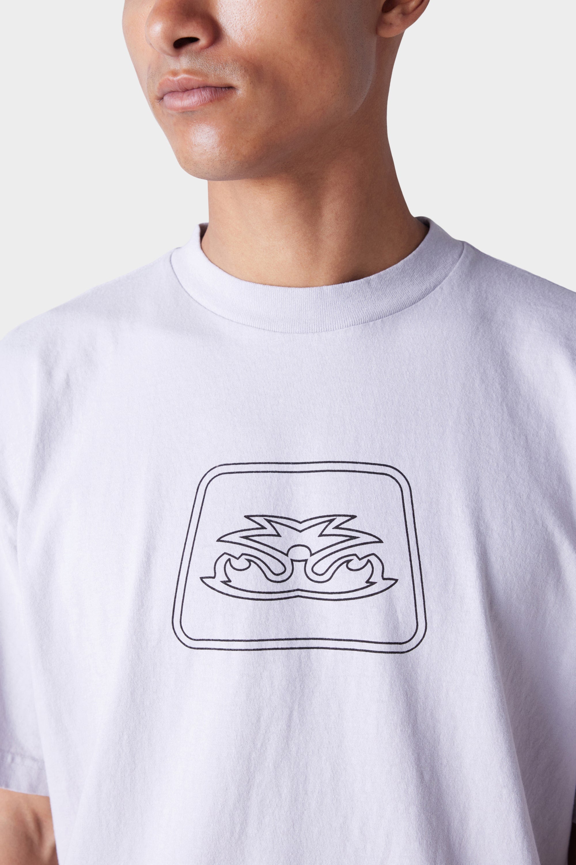 A person wears the 686 Mens Jib Flower Outline Short Sleeve Tee—a plain white T-shirt by 686 with a simple black abstract line drawing on the chest. The background is plain and they are looking slightly to the side.