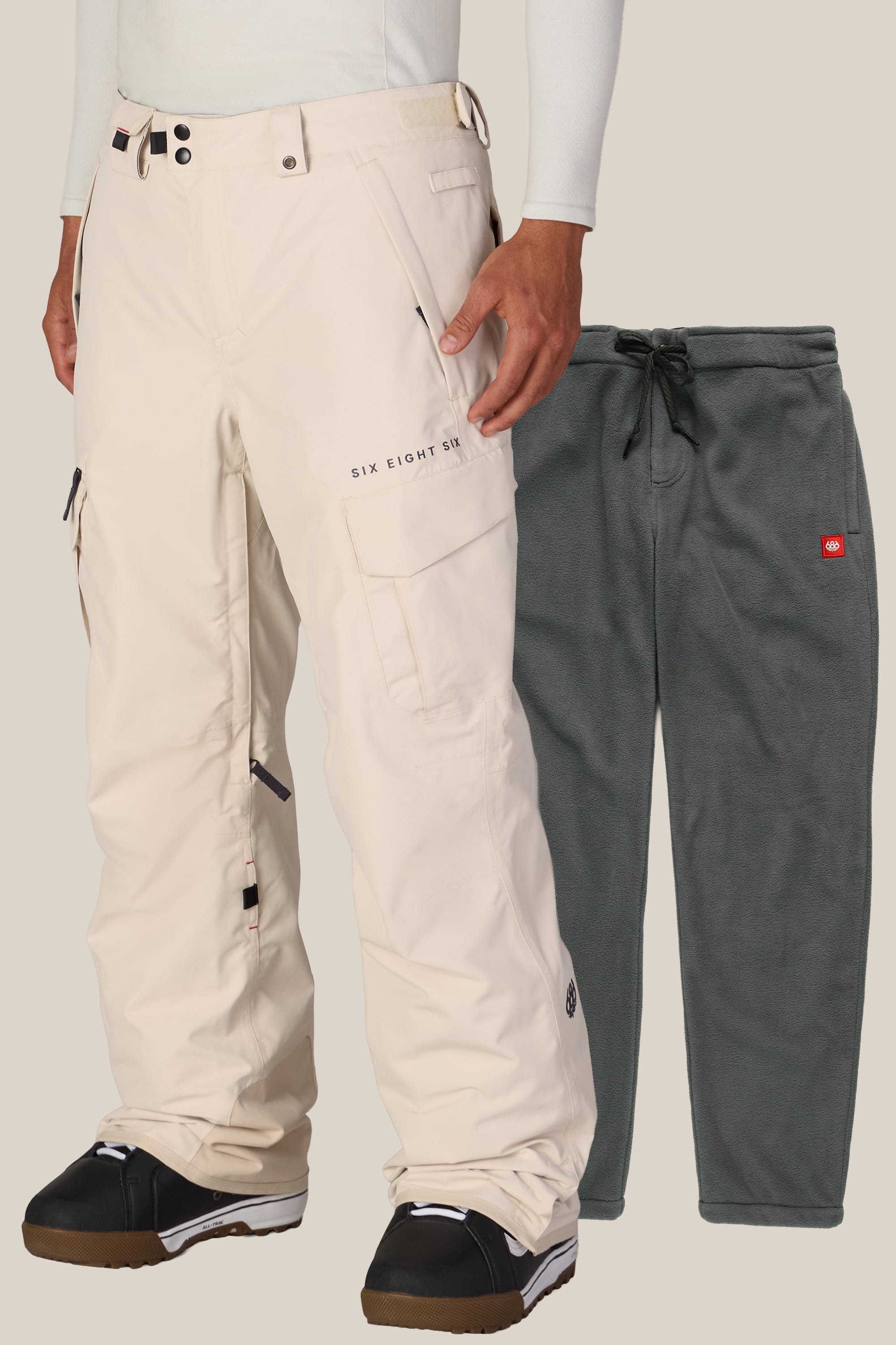 A person wears 686 Men’s SMARTY® 3-in-1 Cargo Pant in beige and black boots, standing next to a pair of dark green fleece pants with a drawstring waist, displayed against a light background.