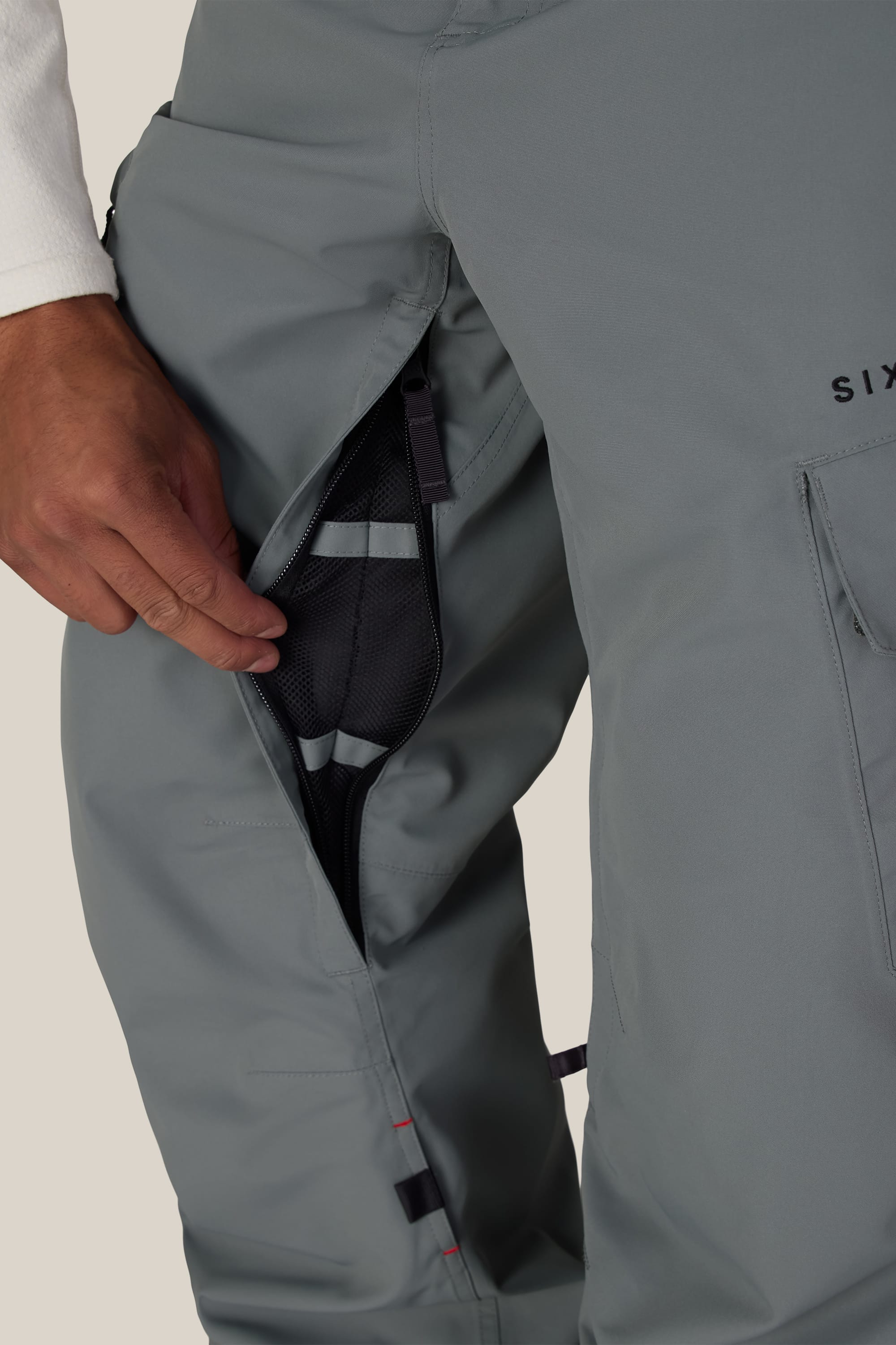 A person unzips a thigh vent on the 686 Men’s SMARTY® 3-in-1 Cargo Pant, revealing mesh lining inside.