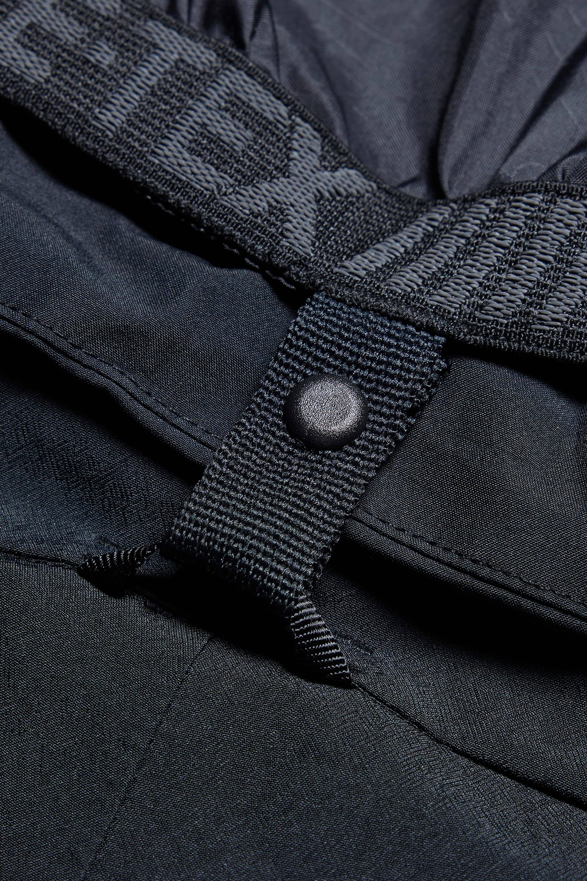 Close-up of the 686 Men’s SMARTY® 3-in-1 Cargo Pant in black, highlighting the stitched strap with a snap button and the elastic waistband with partially visible branding.