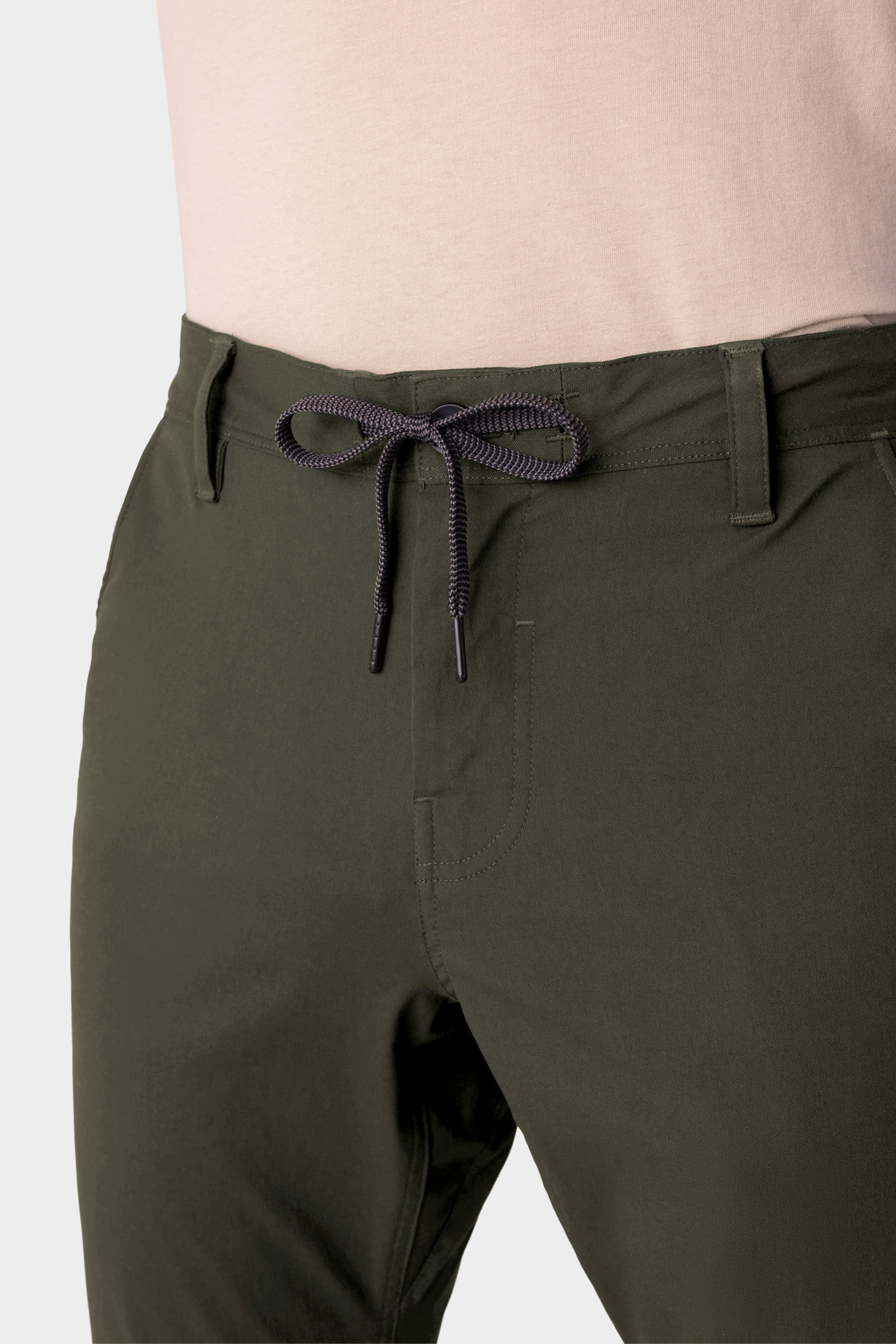 A person wearing 686 Men's Everywhere® Pant - Slim Fit in olive green with a light pink shirt, shown waist to mid-thigh. The breathable pants from 686 feature belt loops and a tied front drawstring.