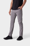 A person wears 686 Mens Everywhere Pant - Slim Fit in light gray, a black t-shirt, and black sneakers, standing with one hand in their pocket against a plain white background.