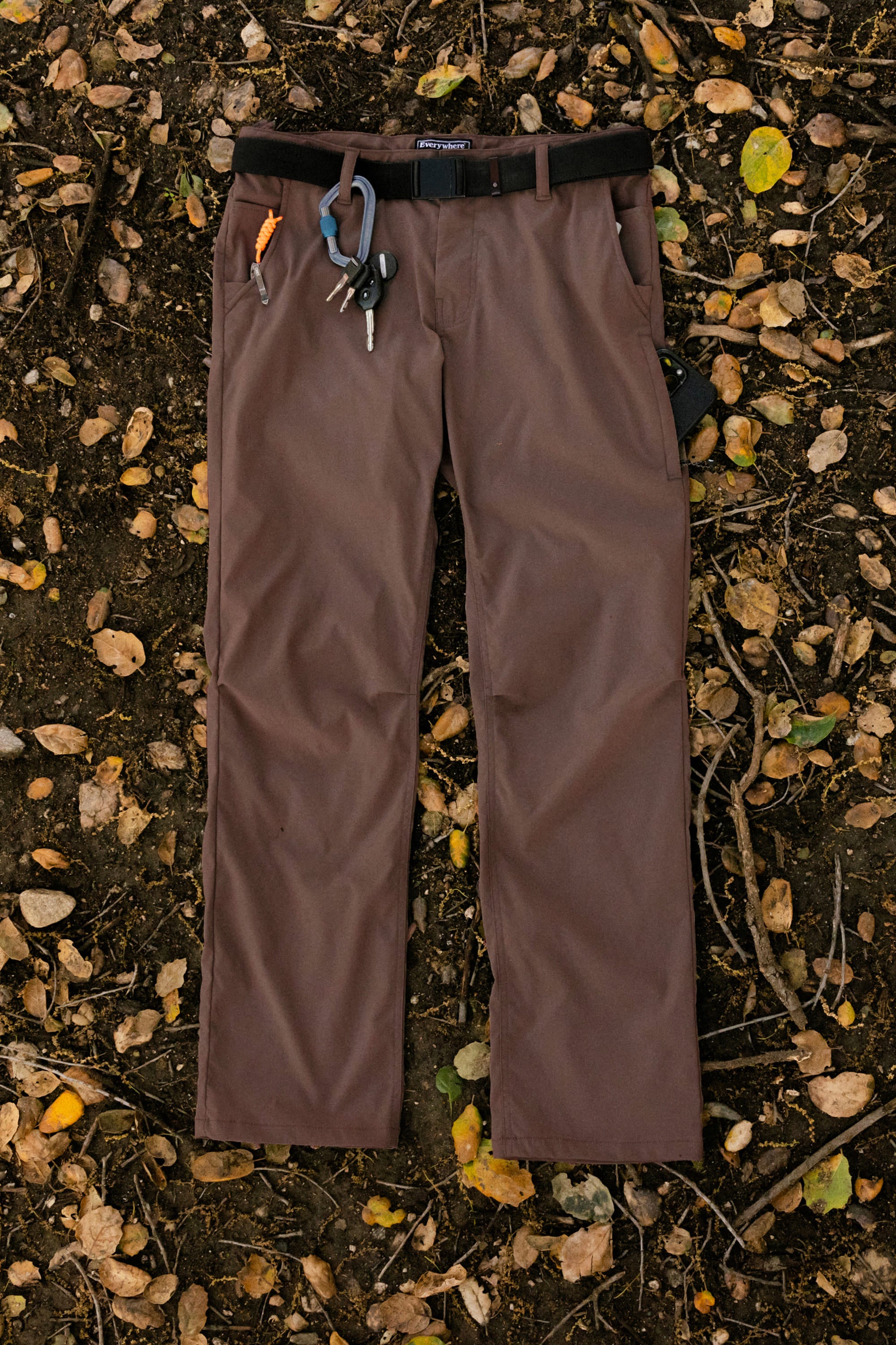 The 686 Men's Everywhere® Pant - Relaxed Fit by 686 features breathable fabric, a black belt, orange and blue carabiners, and keys on the belt loops—perfectly stain-resistant for outdoor adventures among yellow and brown leaves.