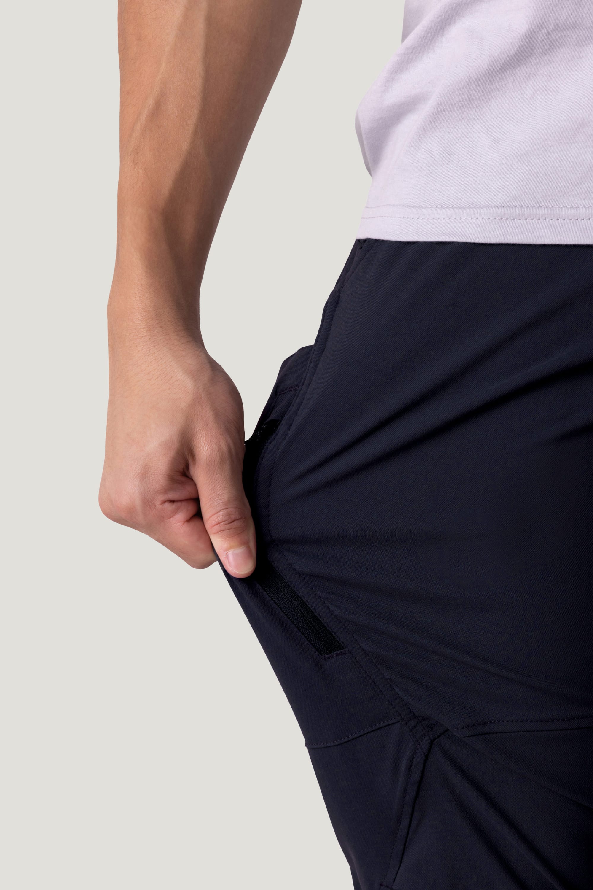 A person reveals a hidden zipper in the side pocket of the 686 Men's Anything Cargo Pant - Slim Fit, wearing a light shirt and ready for adventure against a plain background.