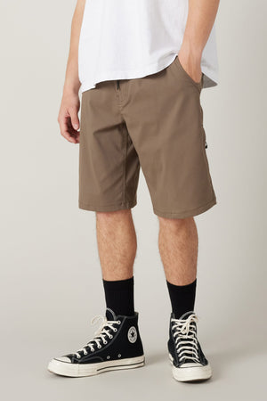 A person stands with hands in pockets against a plain background, wearing a white t-shirt, 686 Men's Everywhere® Hybrid Short - Relaxed Fit by 686, black crew socks, and black high-top Converse sneakers.