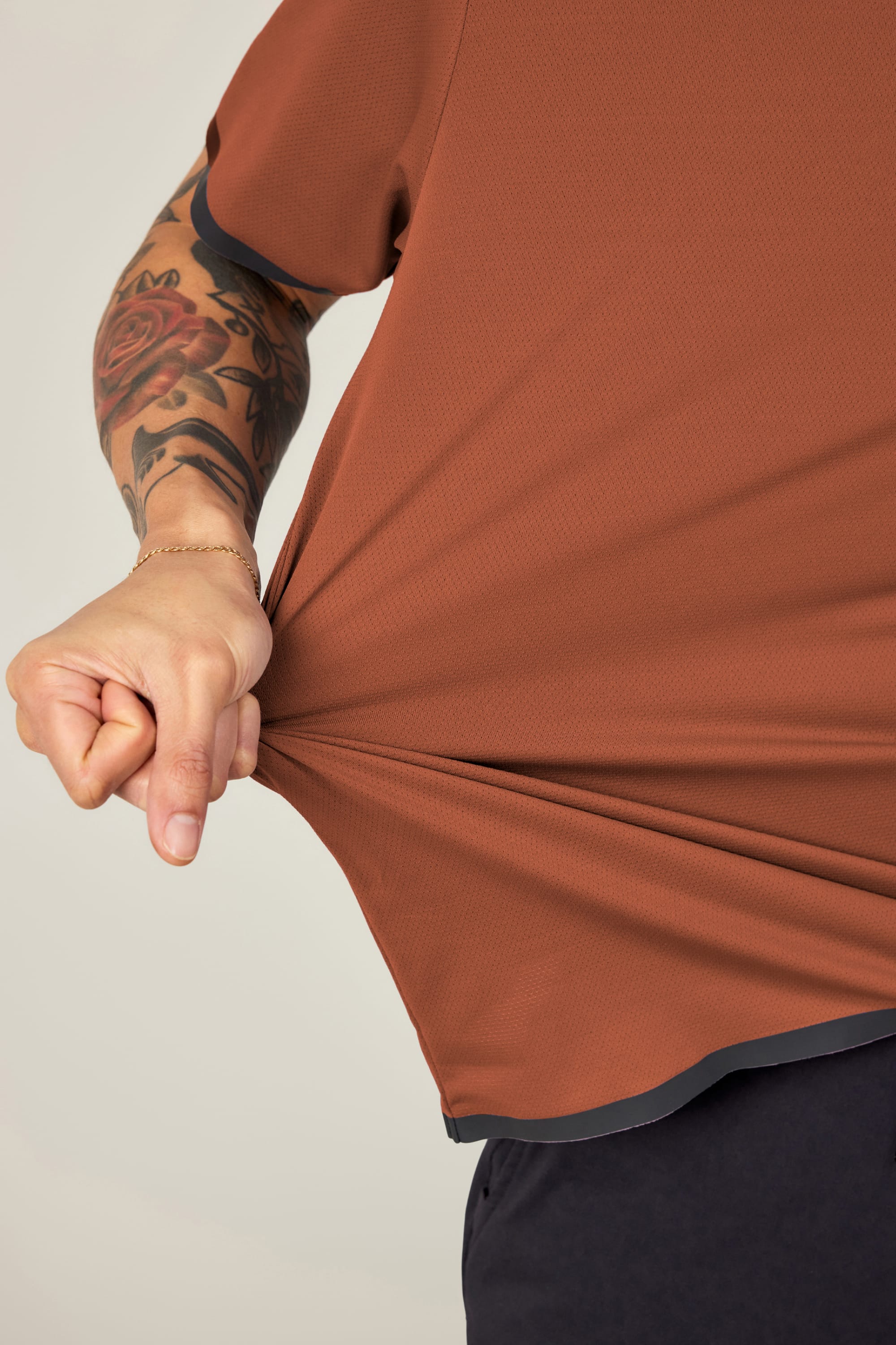 A person with a rose tattoo on their forearm stretches the side of their 686 Men's Let's Go Tech Tee, showing off its flexibility. Only their torso and part of one arm are visible—ideal for spring or summer adventures.
