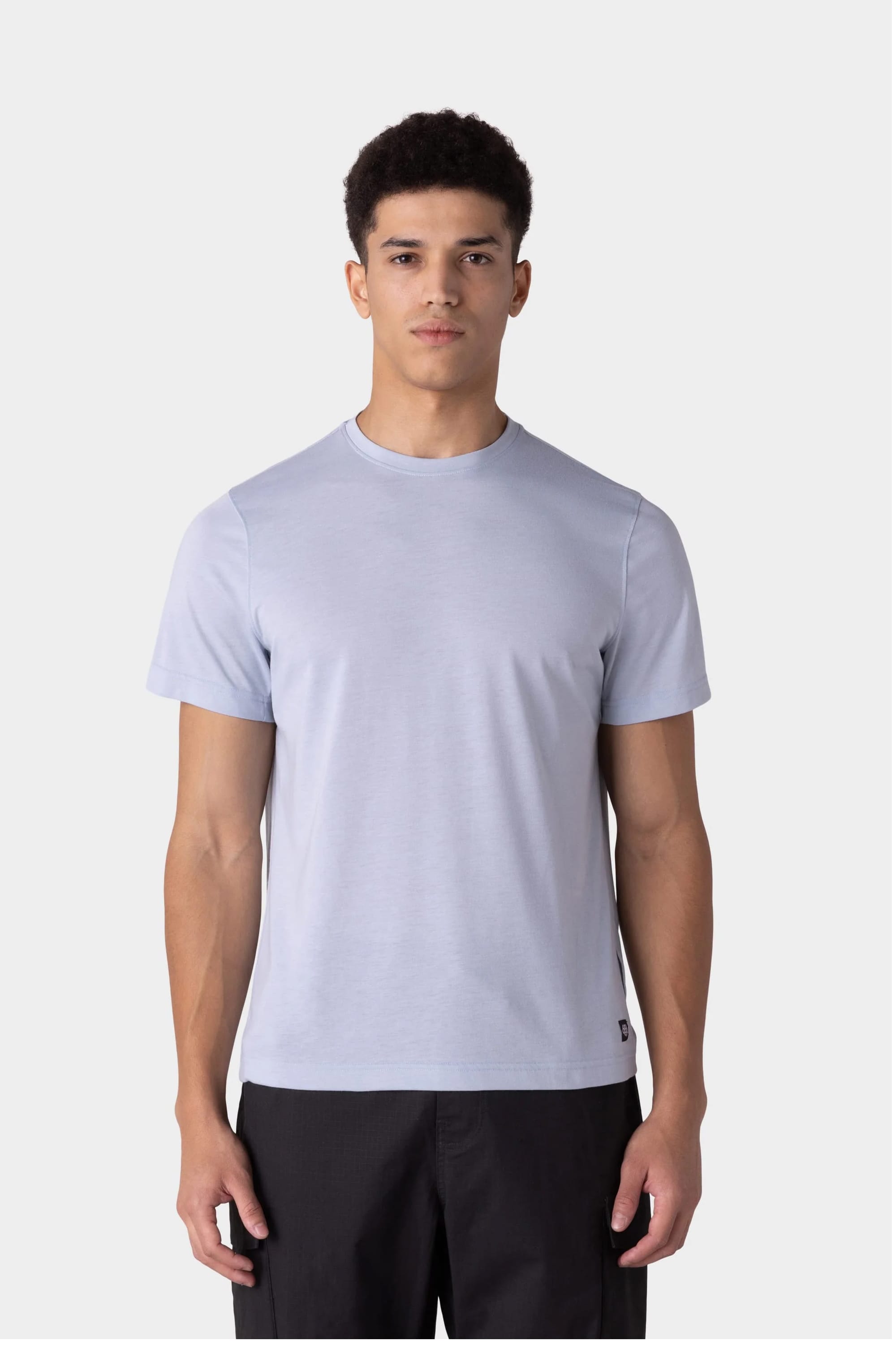 A young man stands facing forward, wearing the 686 Mens Everywhere drirelease® Tech Tee in light gray and black pants against a plain light gray background.
