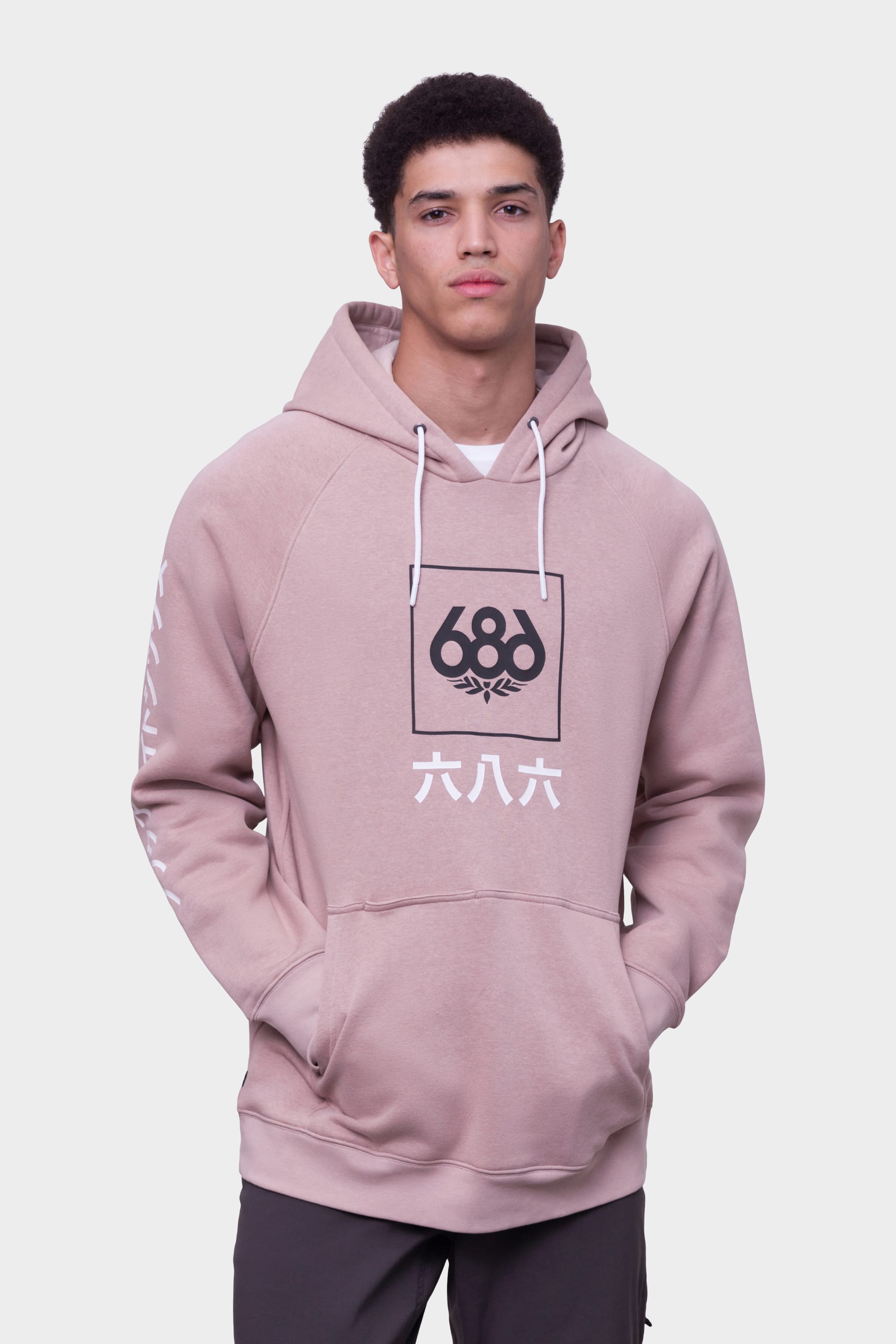 A young man stands with hands in the front pocket, wearing the 686 Mens Script Knockout Hoody featuring the black and white 686 logo and Japanese characters on the front, set against a plain background.