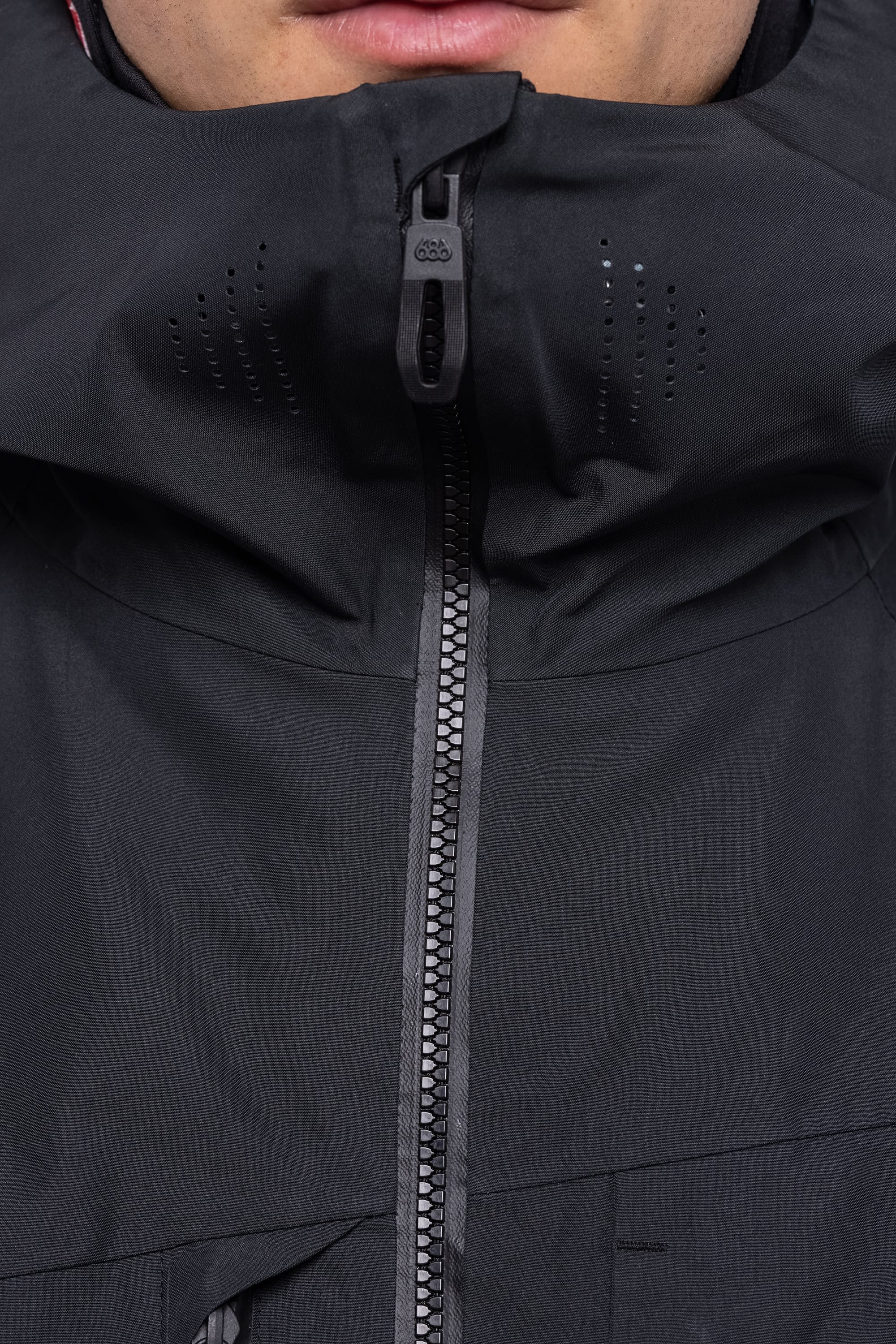 Close-up of a person wearing the 686 Men's Hydrastash Reserve Insulated Jacket, partially zipped to cover their lower face. Only their mouth and chin are visible above the high collar and waterproof fabric.